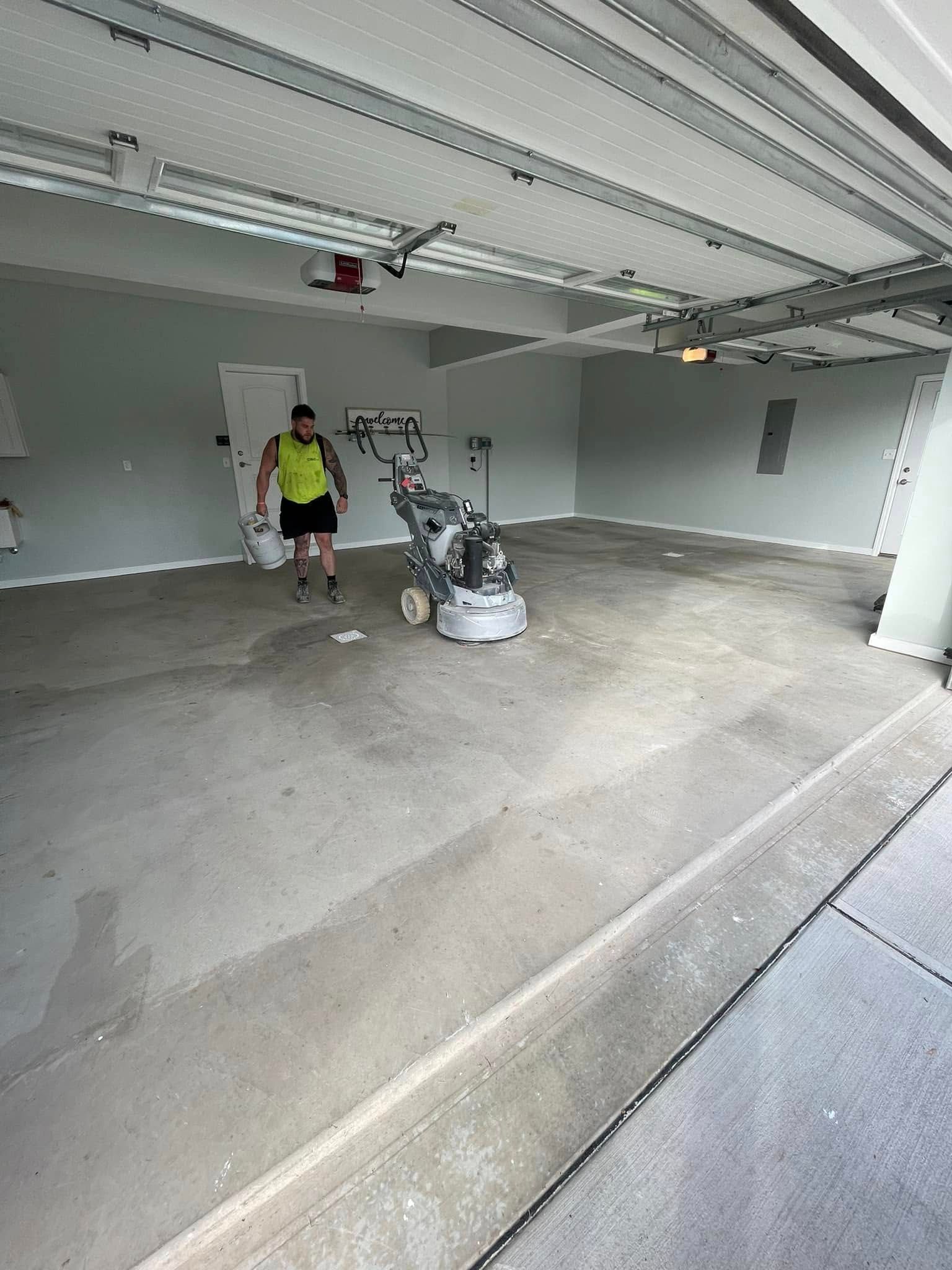 Person standing in a garage next to a motorcycle and a pressure washer on a concrete floor