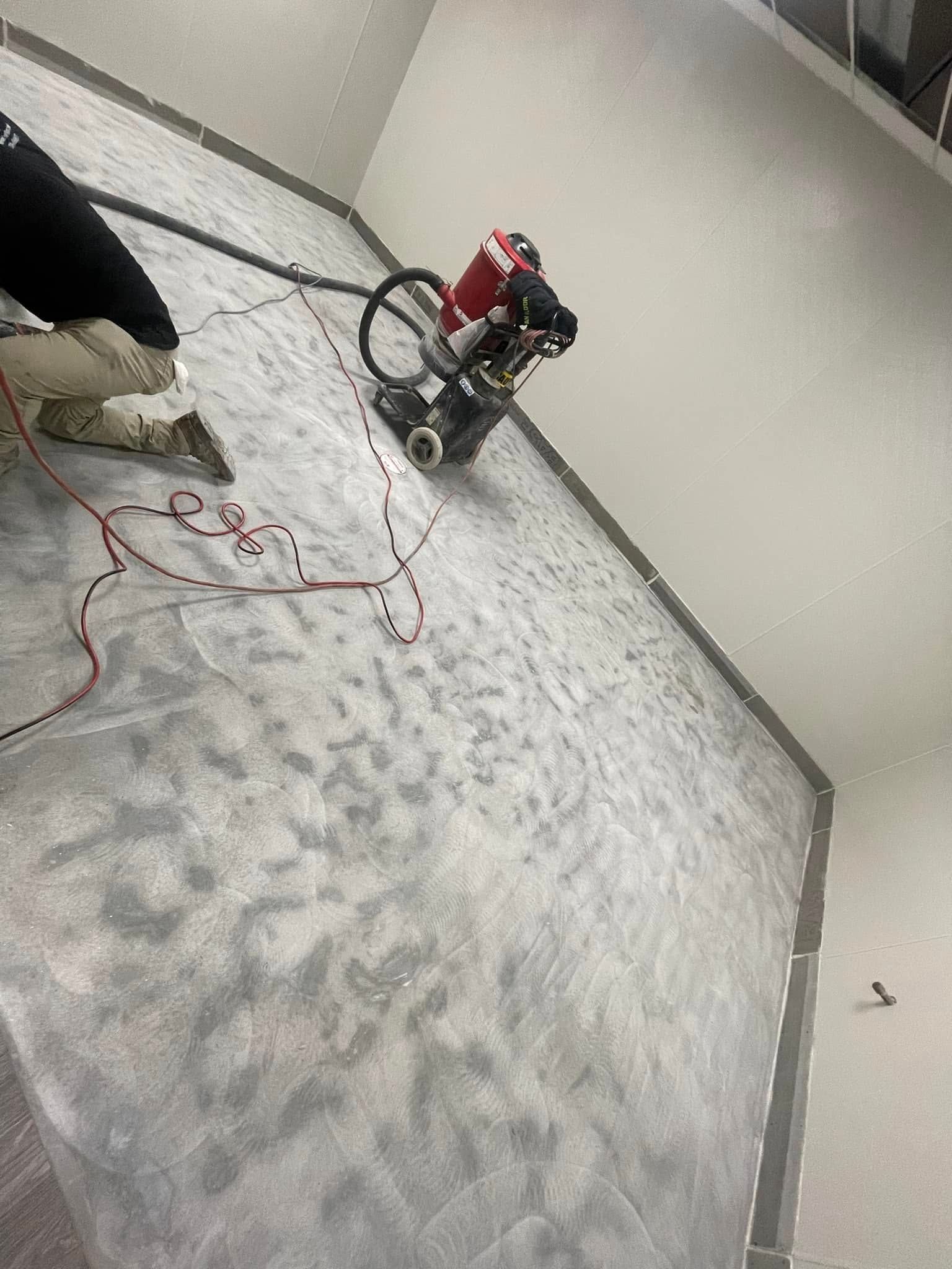Worker operating a floor grinder in a bare room with a gray concrete floor