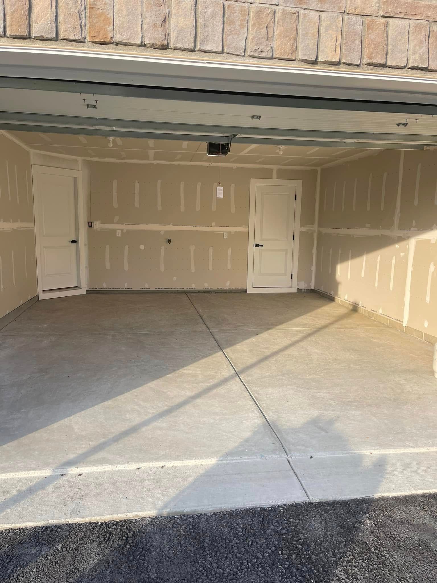 Empty garage with closed white side doors and concrete floor under open garage door
