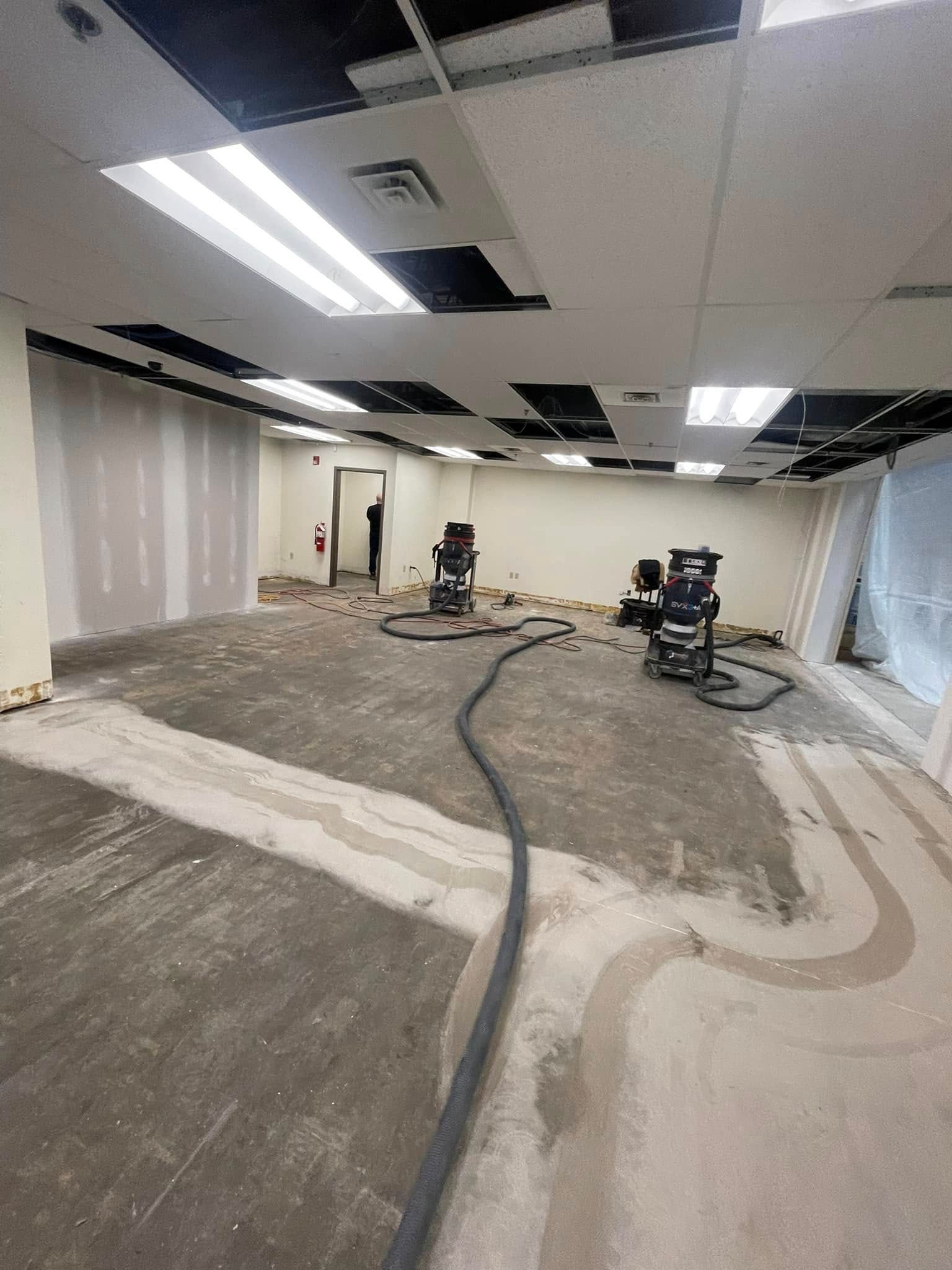 Office space under renovation with unfinished floor, ceiling tiles, and construction equipment