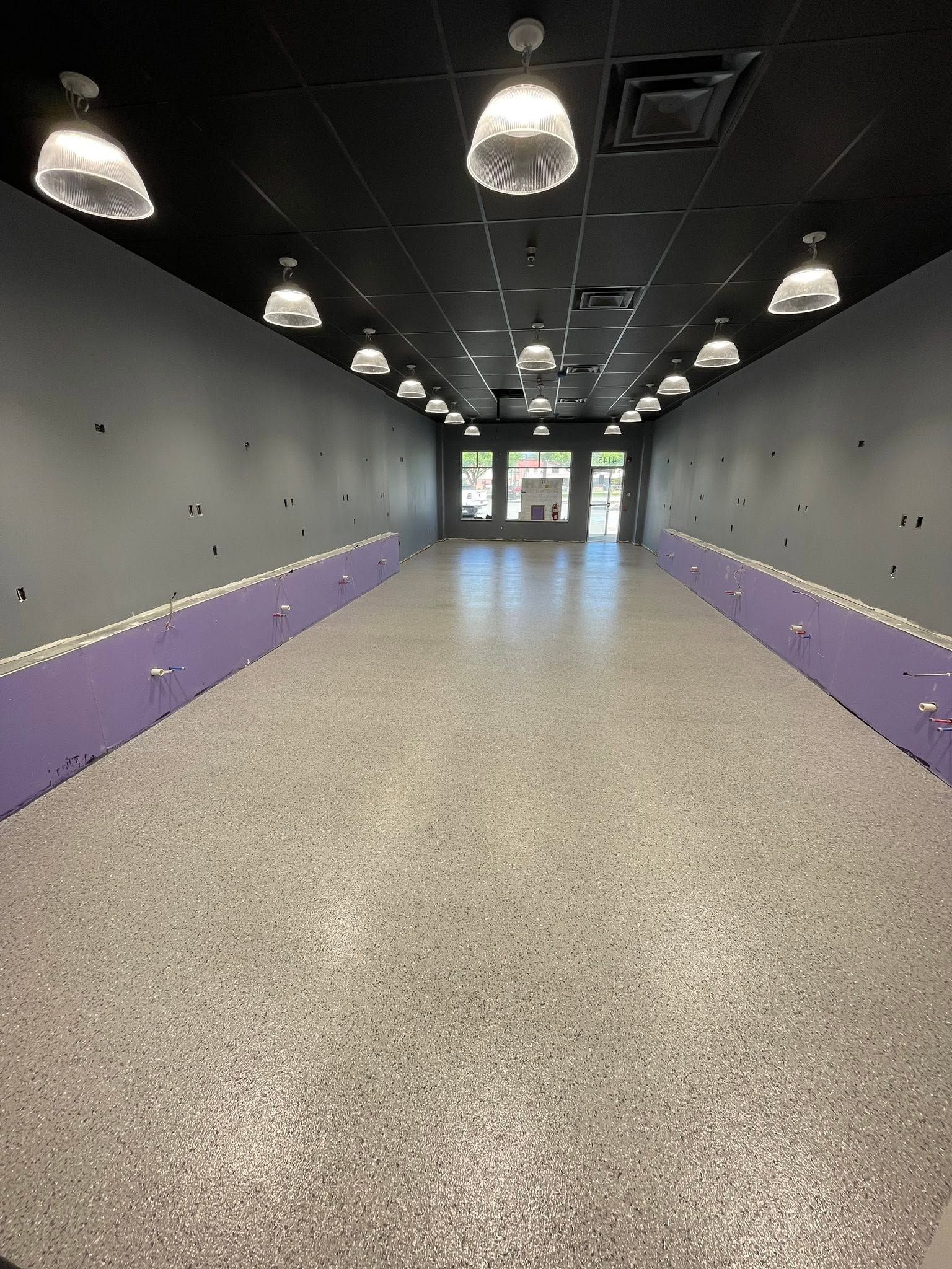 Empty indoor hallway with gray walls, purple accents, and pendant lights leading to glass doors.