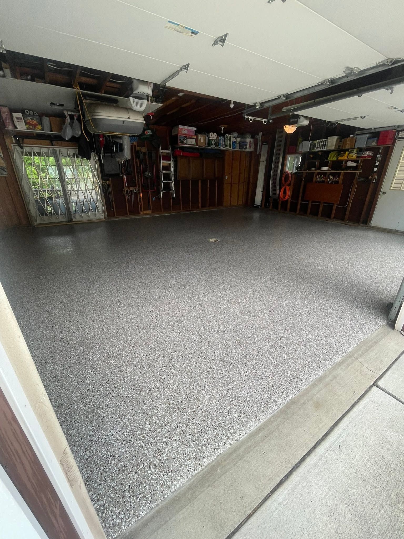 Empty garage with gray speckled floor and open storage cabinets along the walls