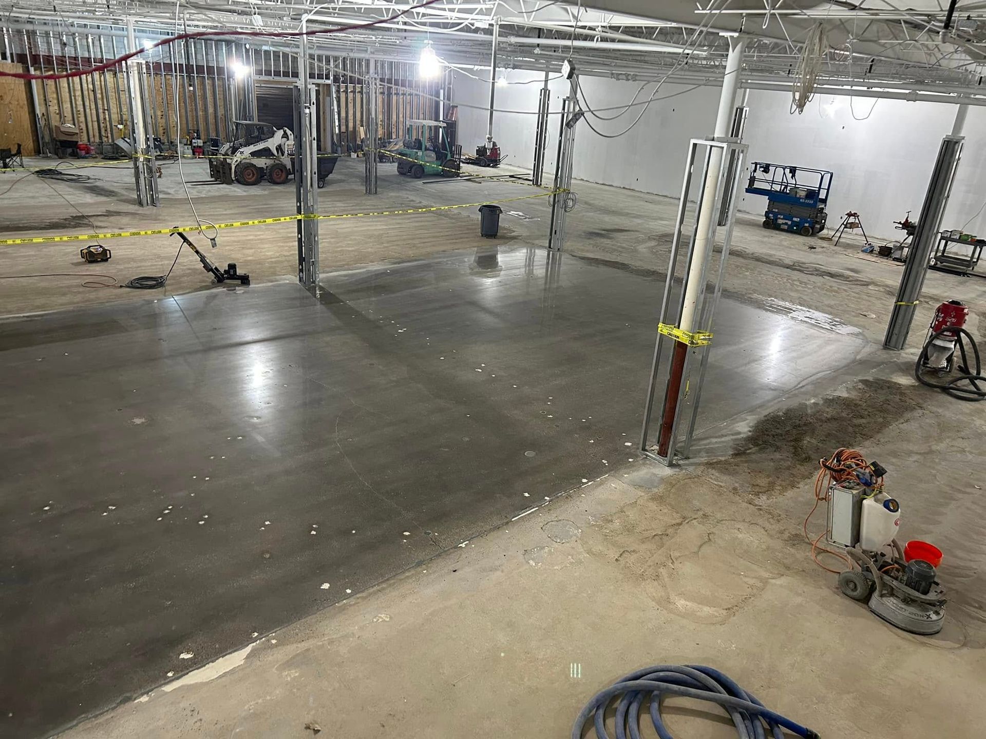 Large unfinished basement with freshly poured concrete floor and construction equipment under exposed beams.