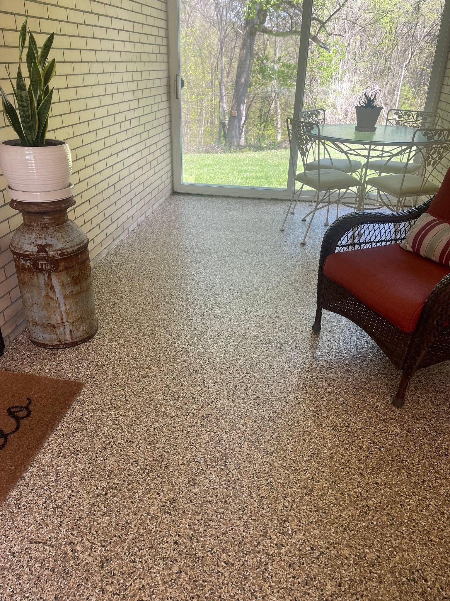Screened porch with speckled floor, wicker chair, potted plant, and glass table overlooking a yard.
