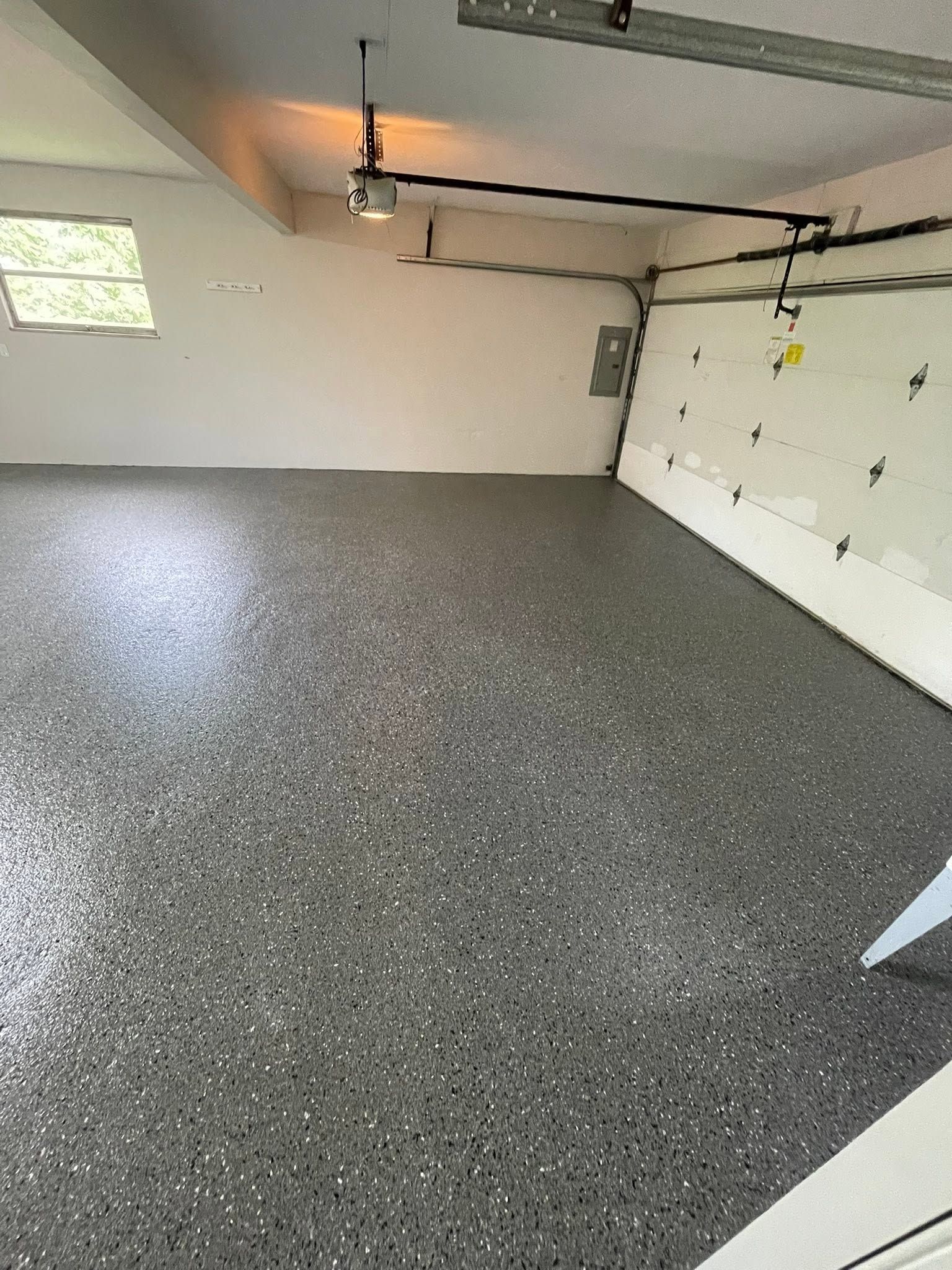 Empty garage with speckled epoxy floor, white walls, and a closed garage door.