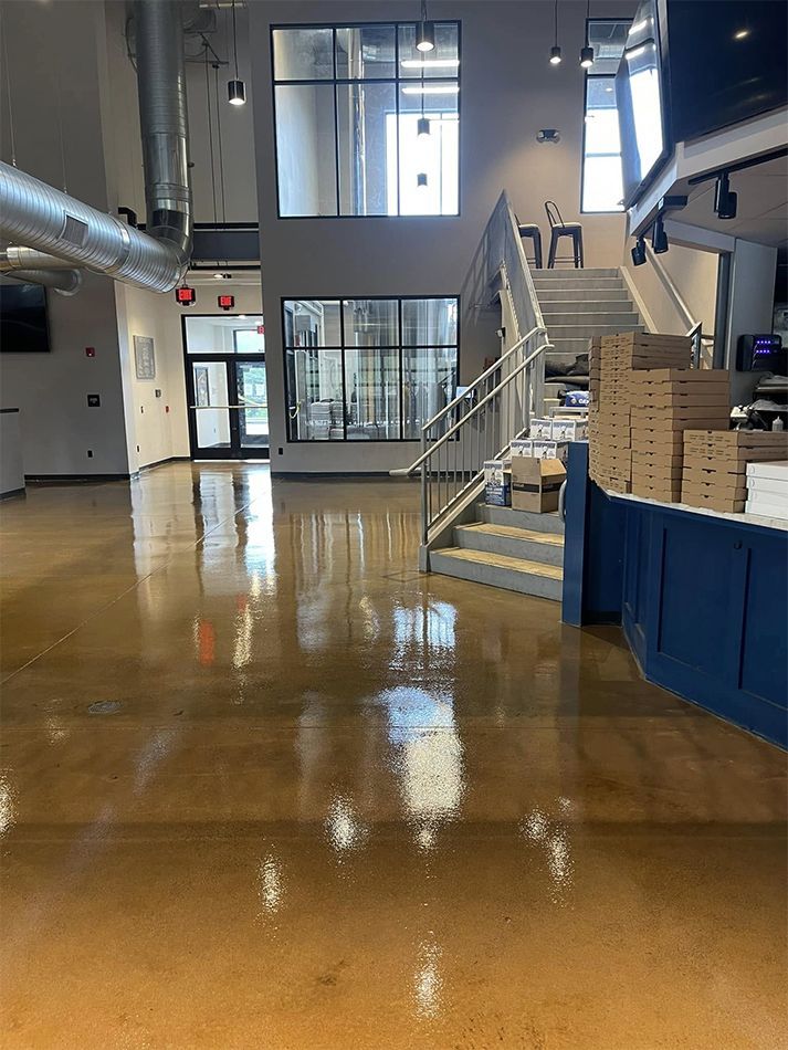 Empty indoor lobby with glossy floor, stairs, glass doors, and boxes stacked by a blue counter.