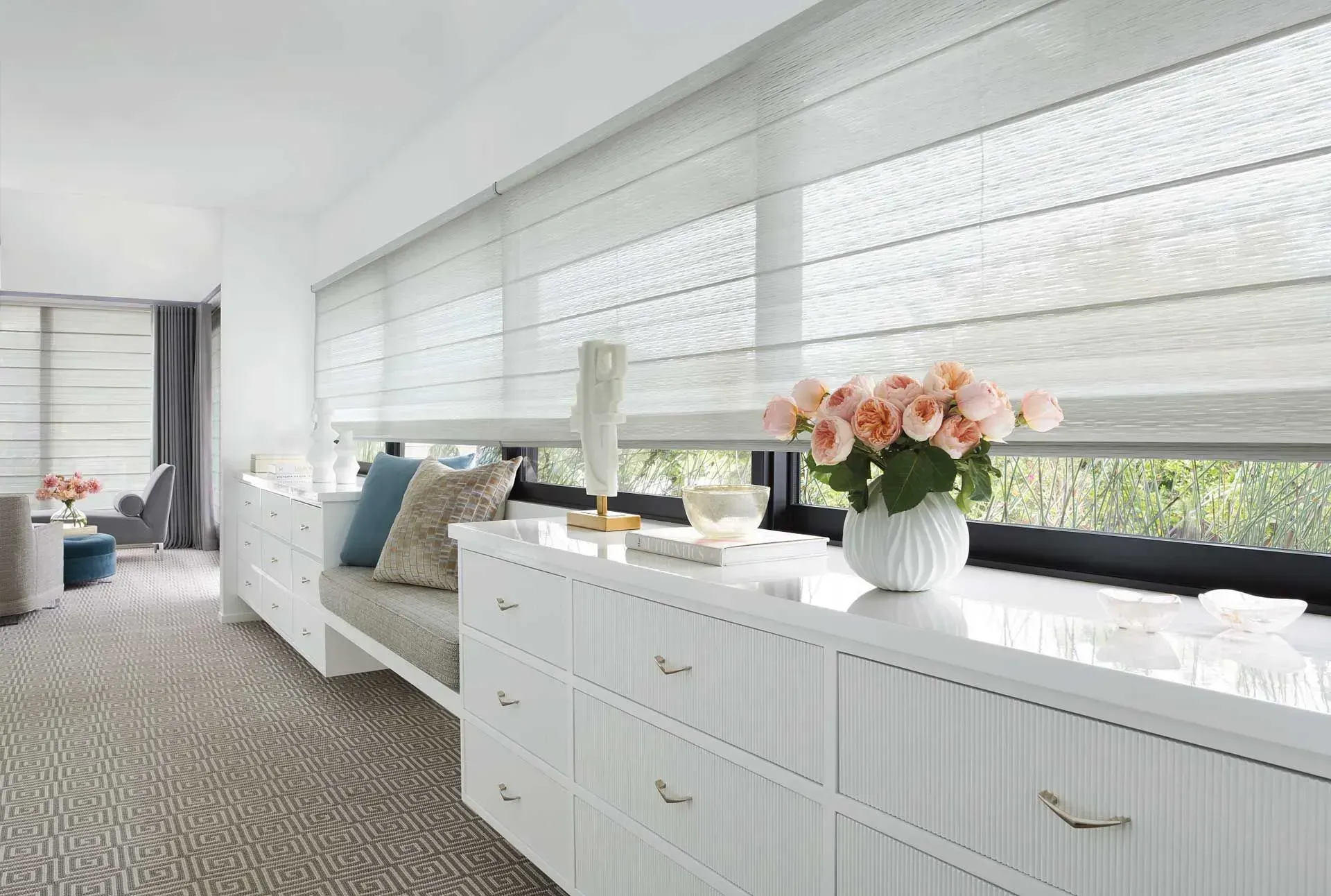 White bedroom interior with long built-in dresser, window seat, and flowers on the windowsill.