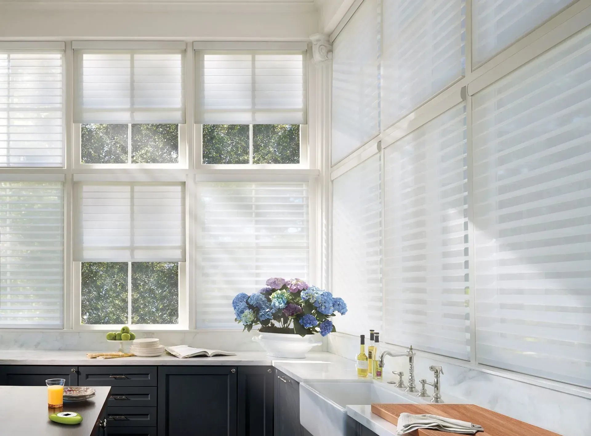 Kitchen with white sheer blinds, dark cabinets, marble countertops, and a flower arrangement.