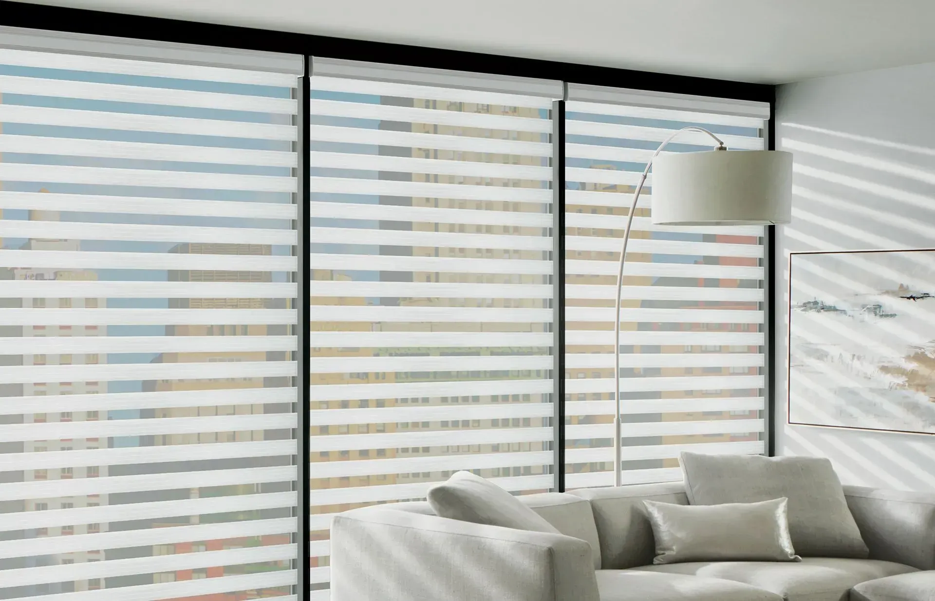 Modern living room with sheer blinds casting striped shadows; sofa, lamp.