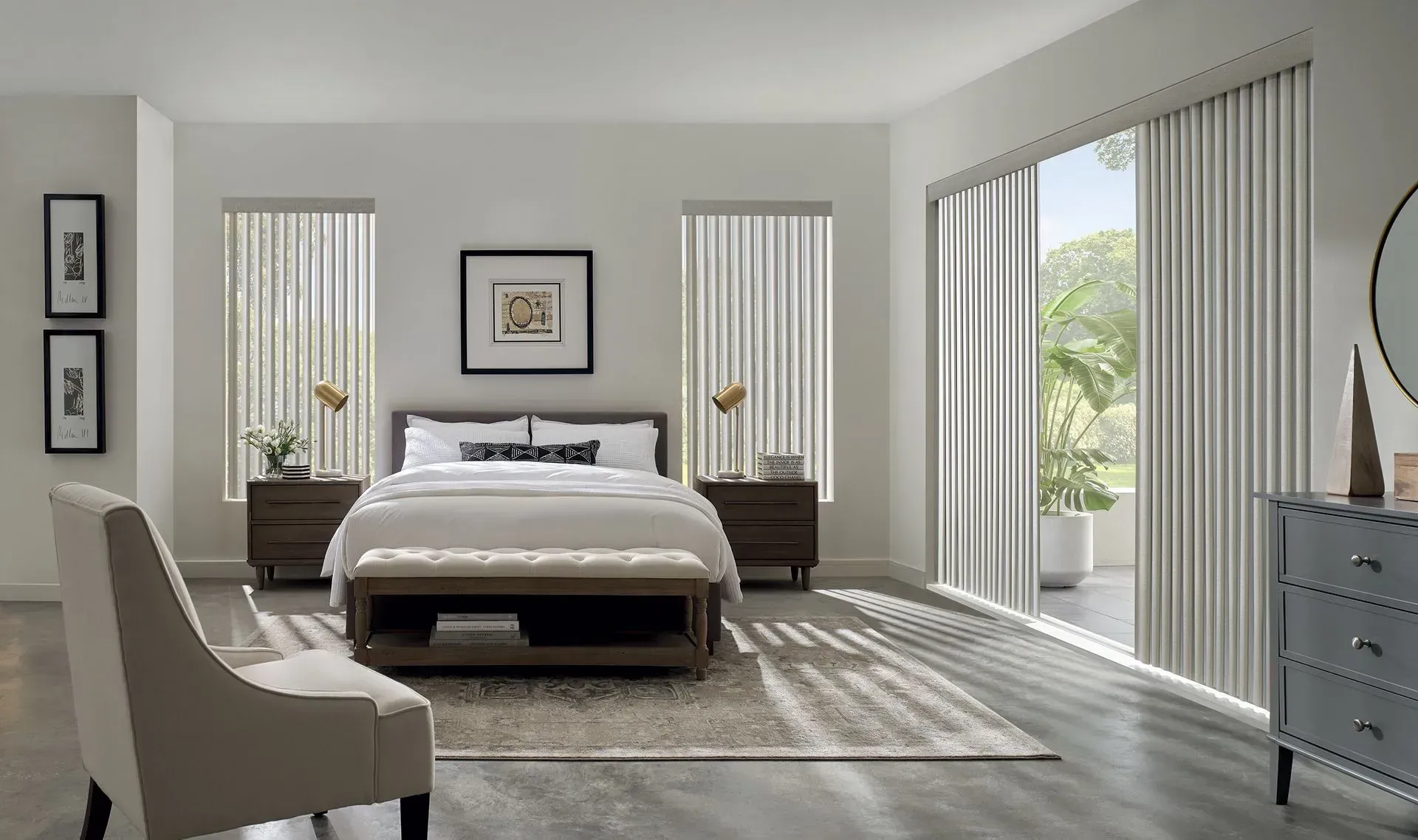 Bedroom with light-colored walls, bed, vertical blinds, sliding door, and a chair. Sunlight streams in.