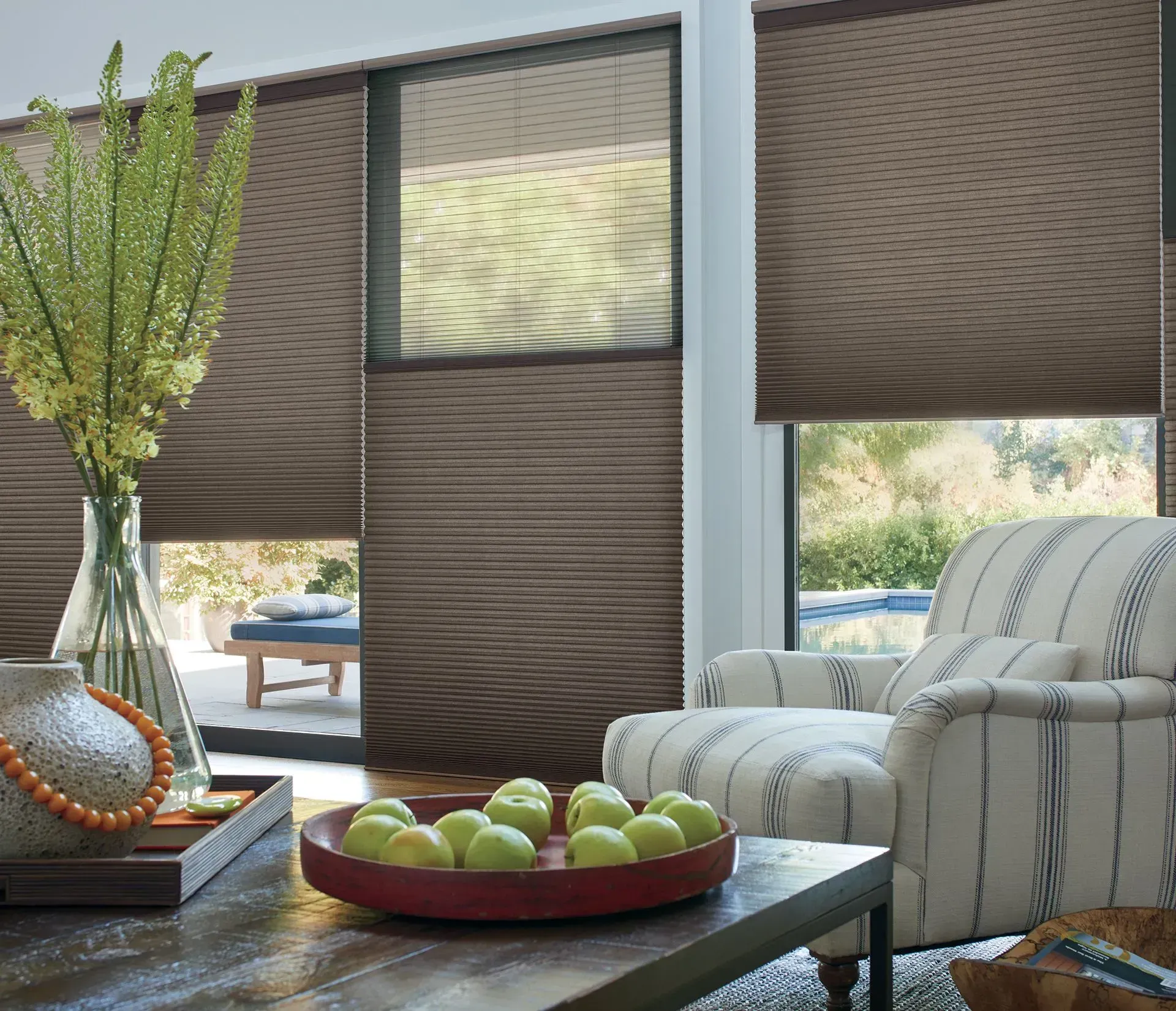 Living room with brown pleated shades, a table with fruit, and a striped armchair.
