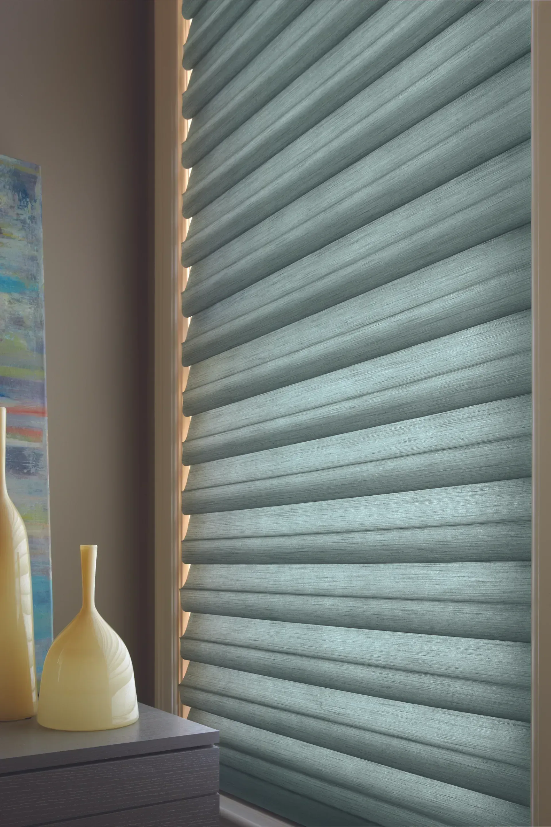 Blue pleated window blinds in a window with a neutral-colored wall and decorative vases on a nearby surface.