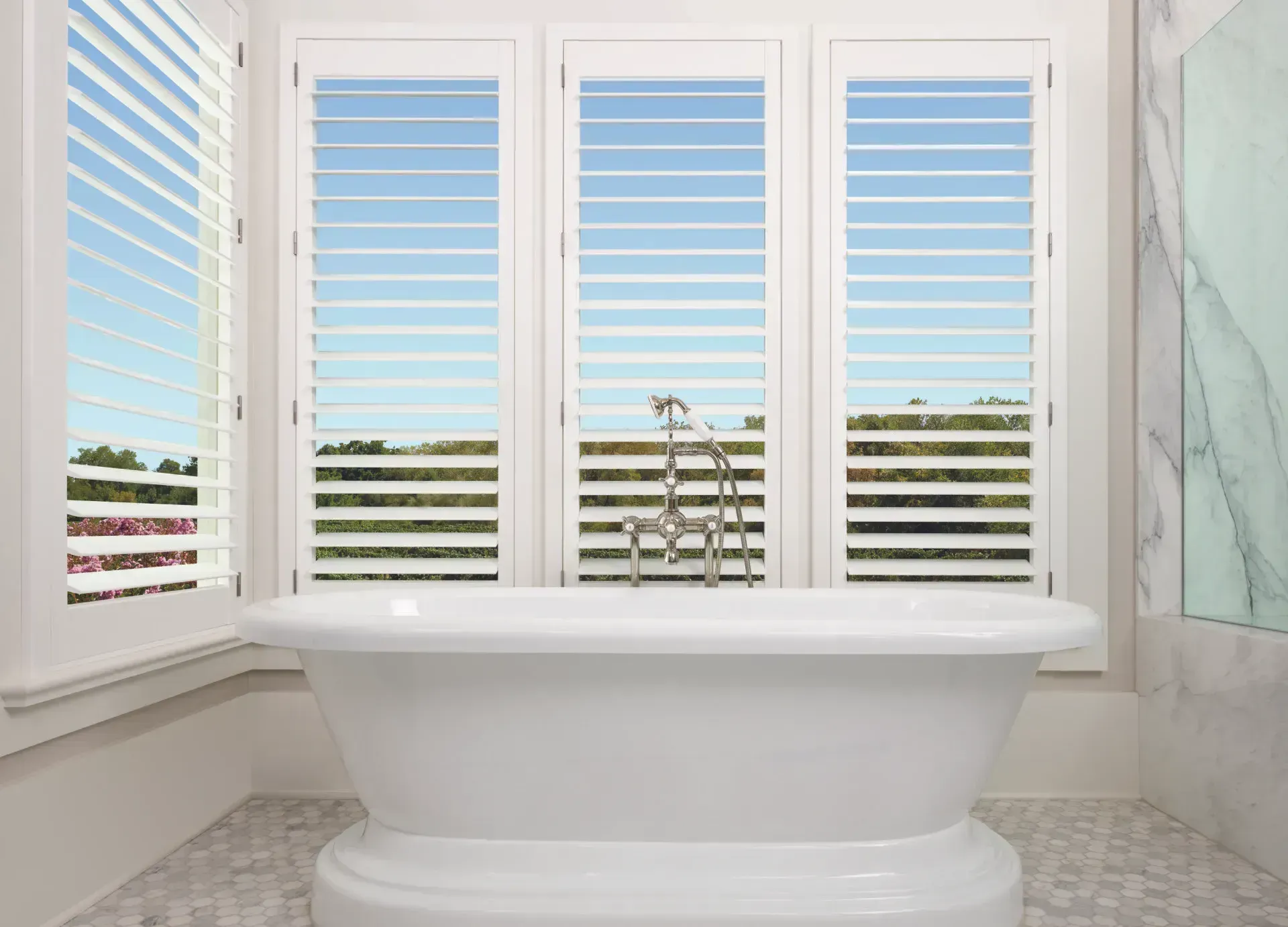 White bathtub in bathroom with shutters and view of the outside.