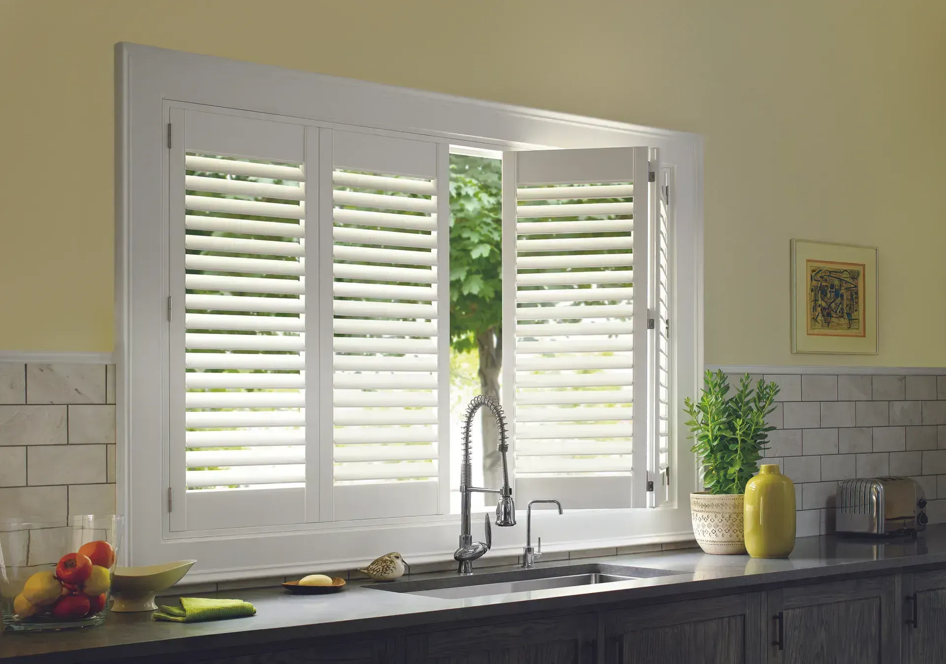 White shutters open over a kitchen sink, framing an outdoor view.