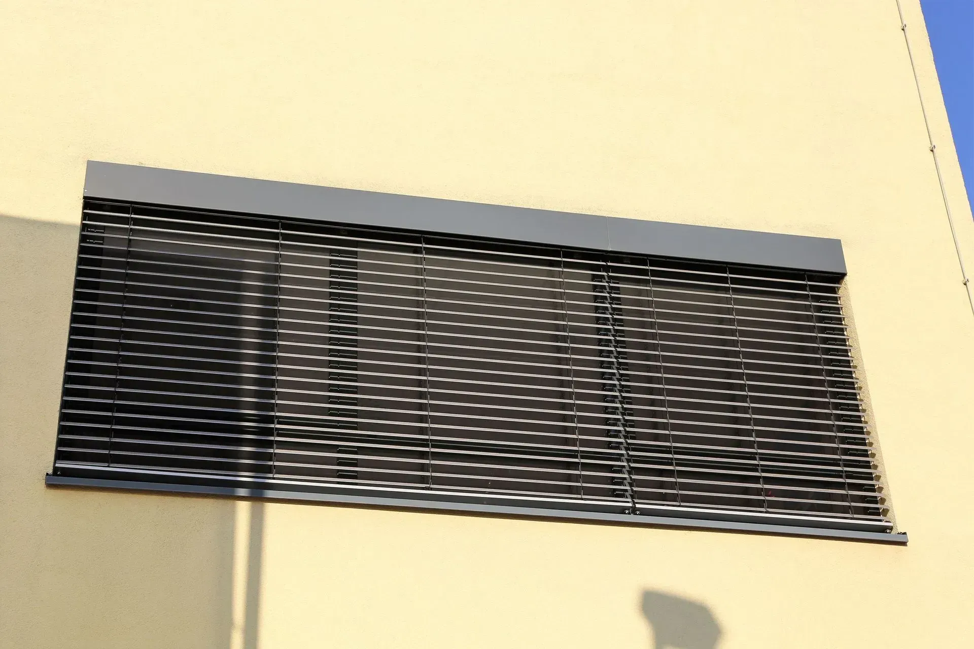 Exterior of a building with a window covered by a closed, dark-colored roller shutter.