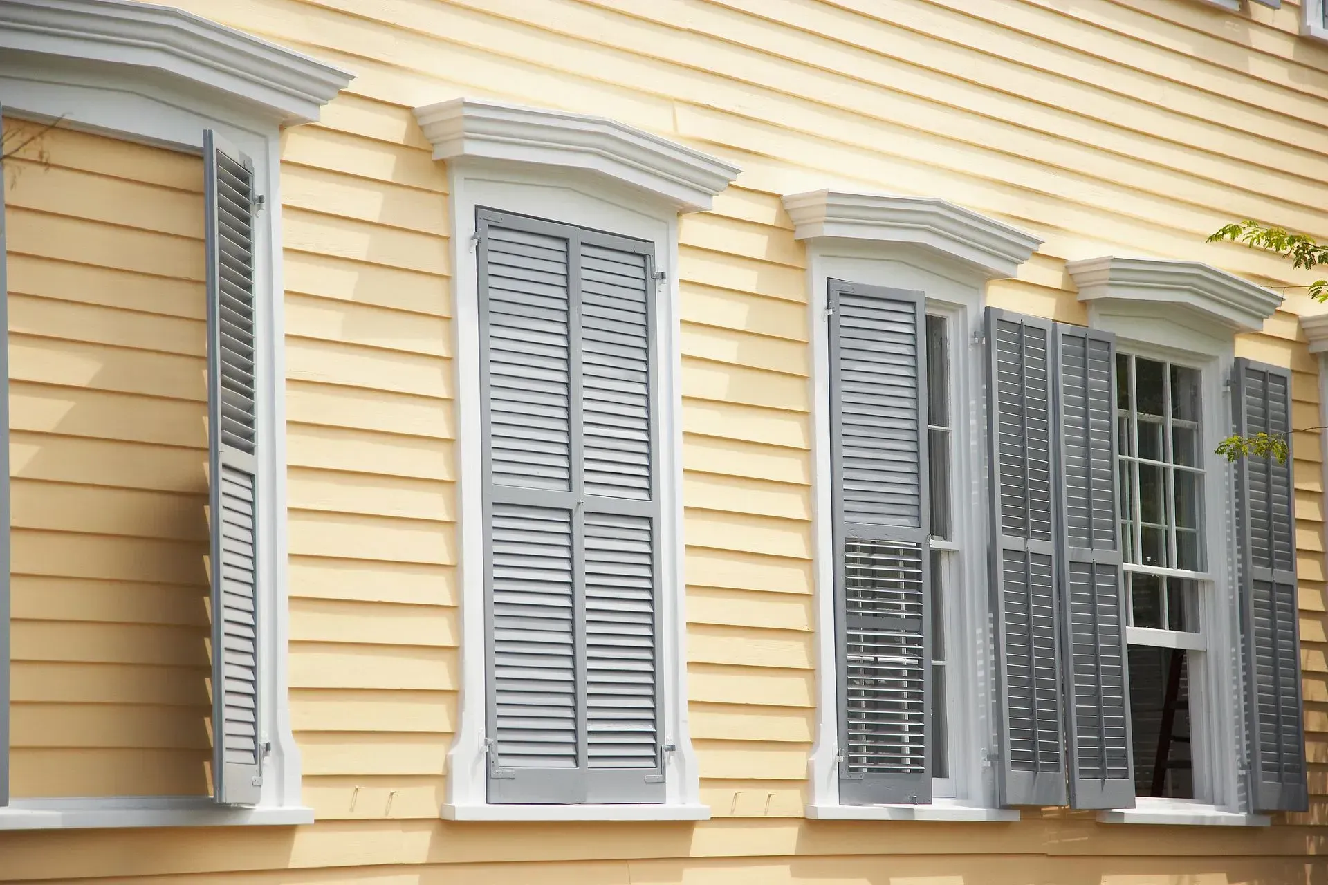 Yellow siding and gray shutters on windows of a historic building.