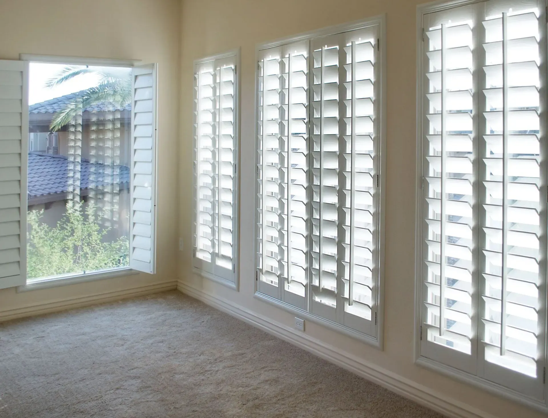 Room interior with beige carpet, white shutters on multiple windows, and a partially open window.