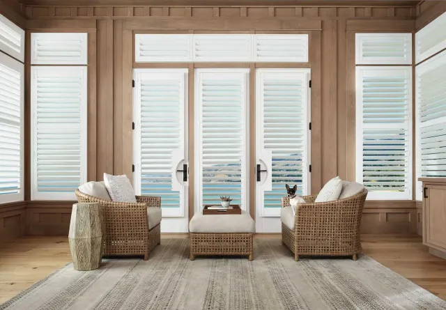 Living room with shutters, wicker chairs, and ocean view. Dog sits in a chair.