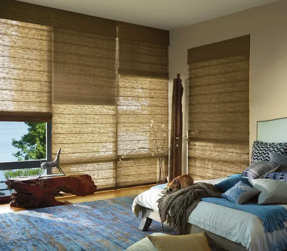 Bedroom with woven blinds, blue rug, and bed with pillows. Dog rests on the bed.