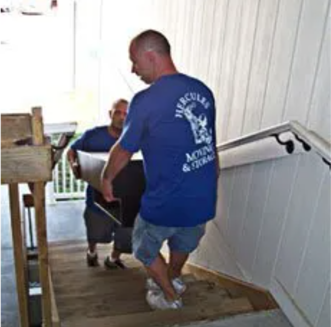men wearing blue shirts moving furniture up a staircase