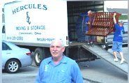 a man is standing in front of a moving Hercules Moving & Storage truck.