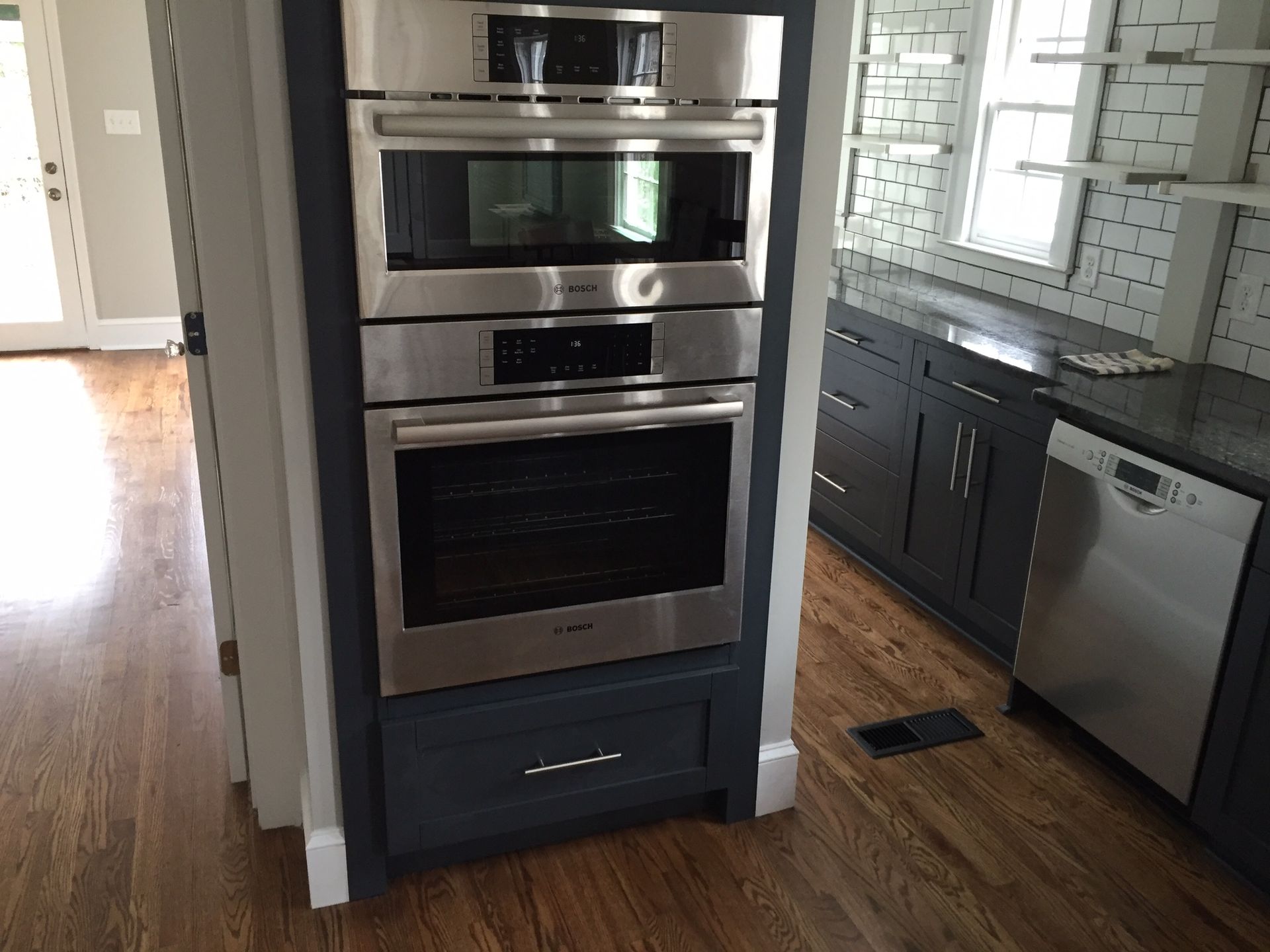Modern kitchen with stainless steel double ovens, dark cabinets, and hardwood floors.