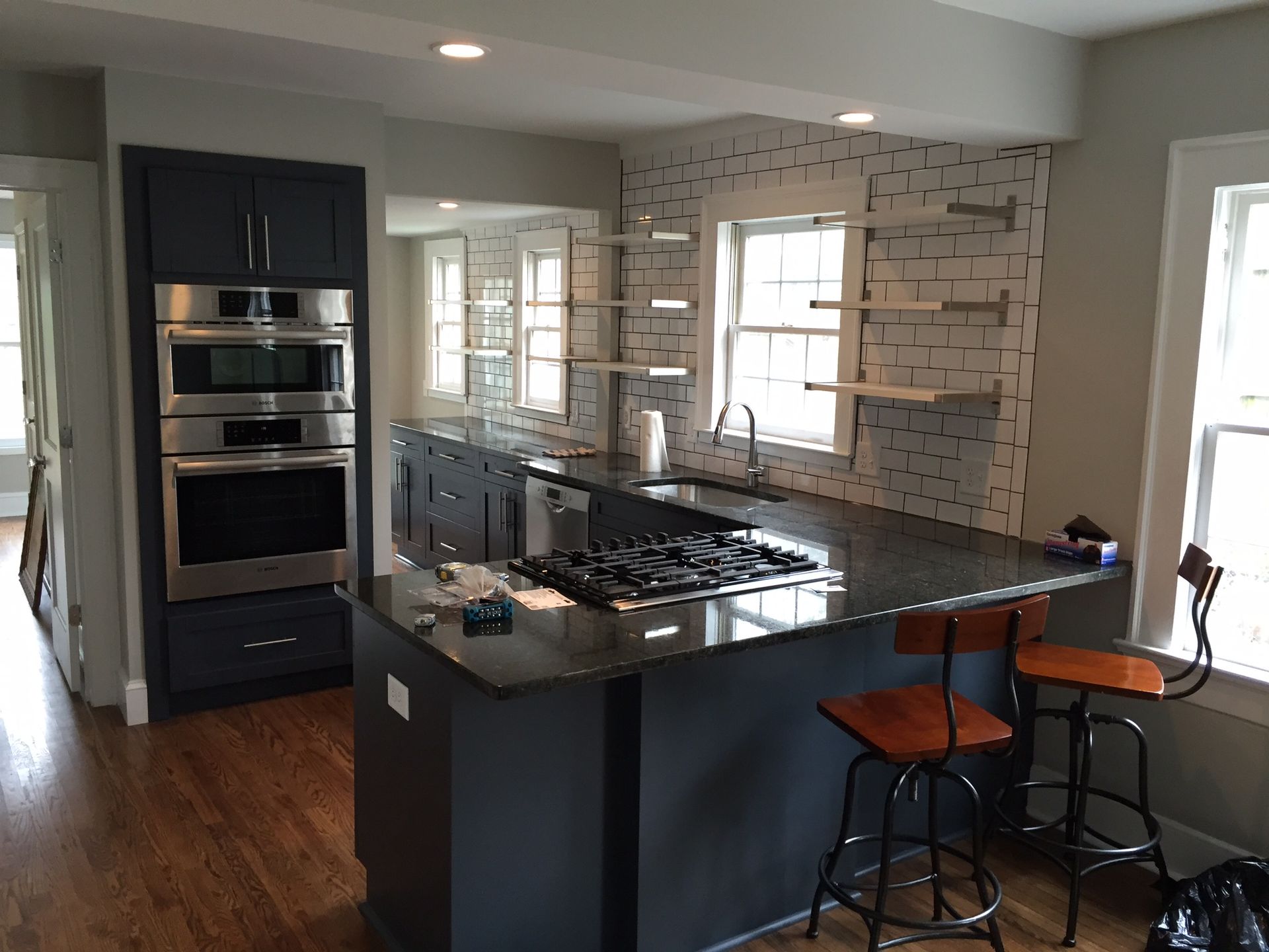 Modern kitchen with dark cabinets, a large island, and bar stools by a windowed backsplash.