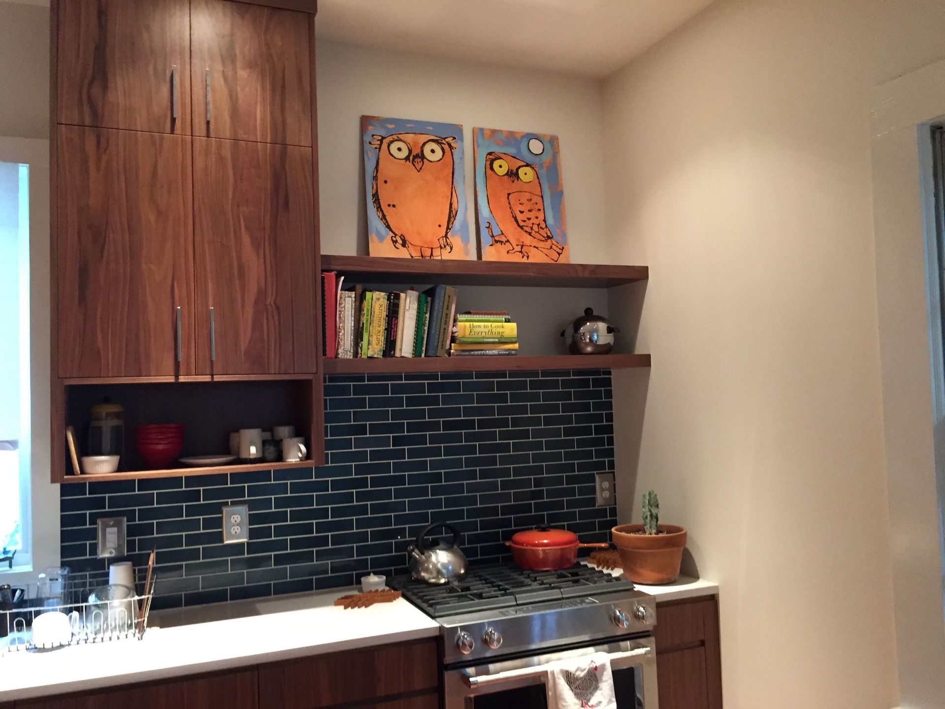 Modern kitchen with dark cabinets, black tile backsplash, open shelves, and orange artwork above the stove.