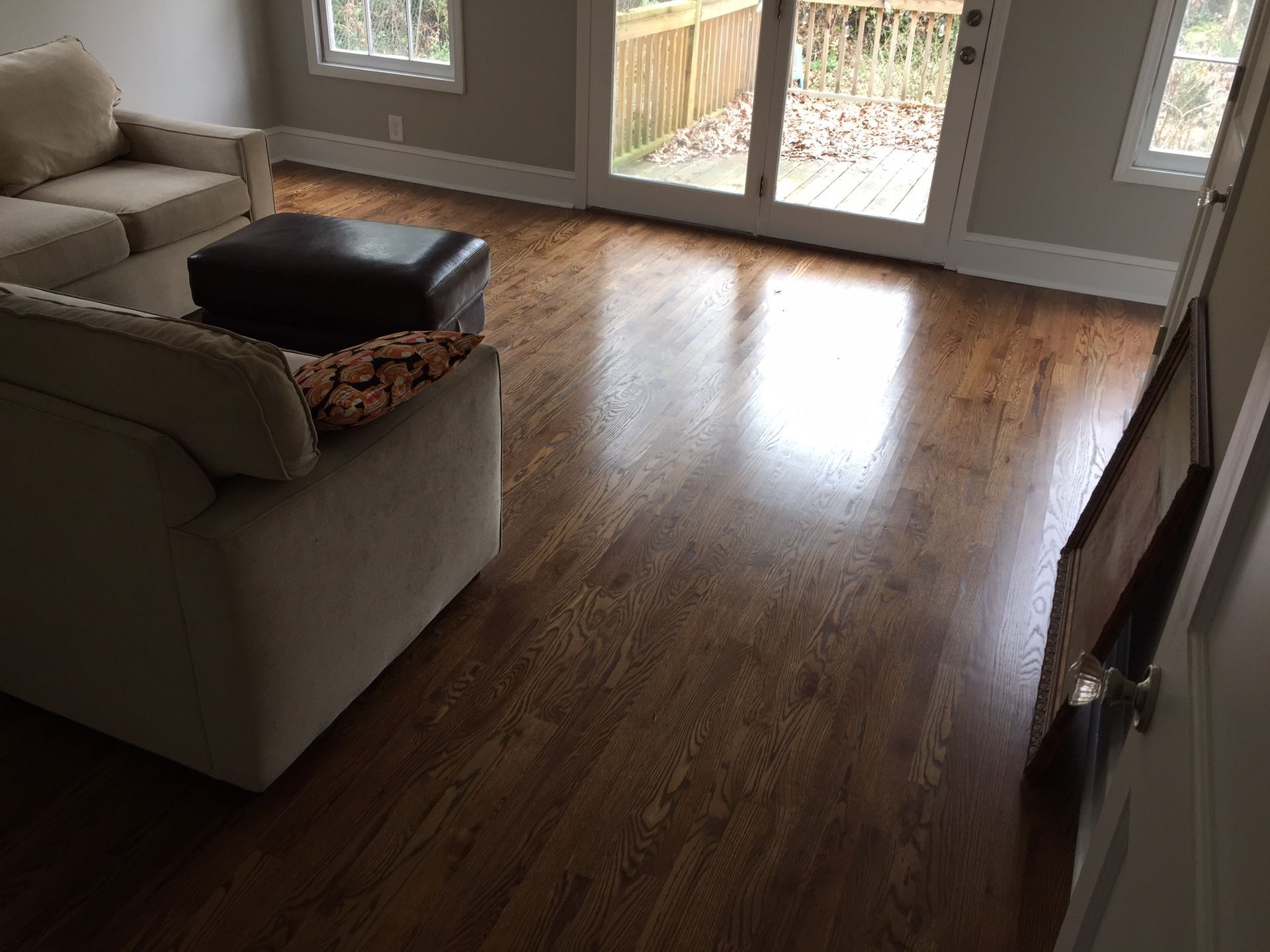 Living room with hardwood floors, beige sofa, ottoman, and sliding glass doors to a patio.