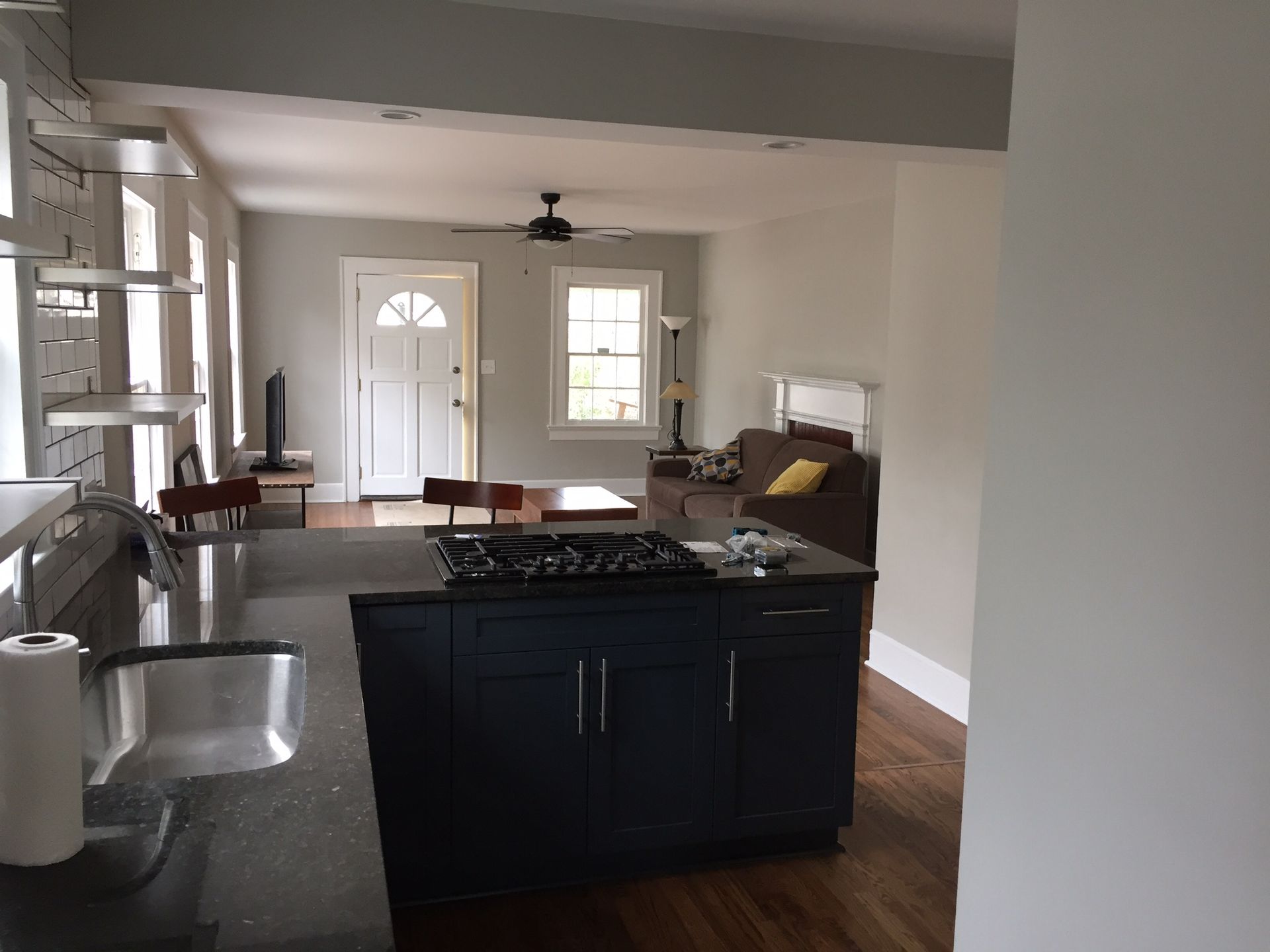 Bright kitchen with black island, sink, and stainless appliances, opening to a living area and front door
