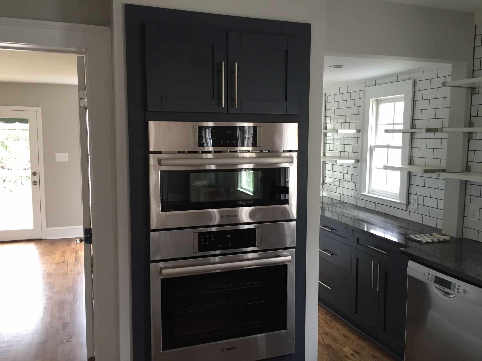Kitchen with dark wood cabinets and stainless steel double wall oven beside a counter and white brick backsplash