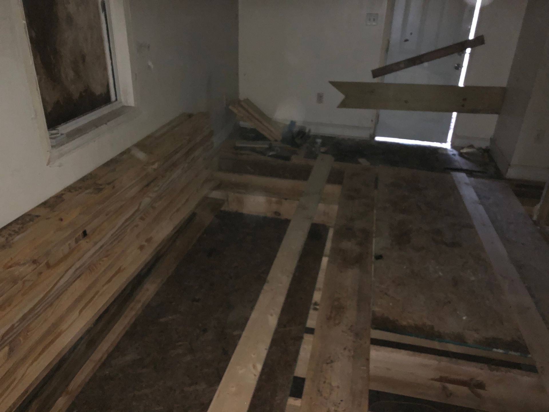 Dim, unfinished room with stacked wooden planks and boards laid across the floor.