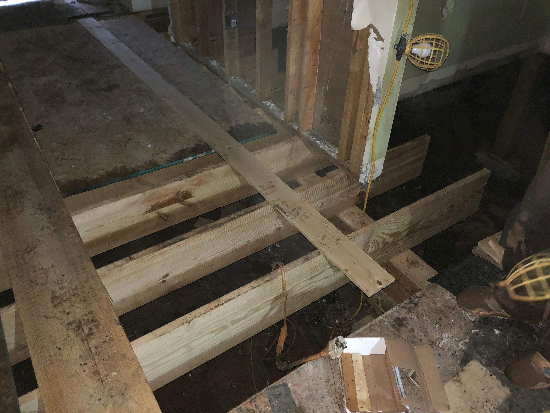 Damaged floor joists exposed in a construction site, with broken wood planks and debris.