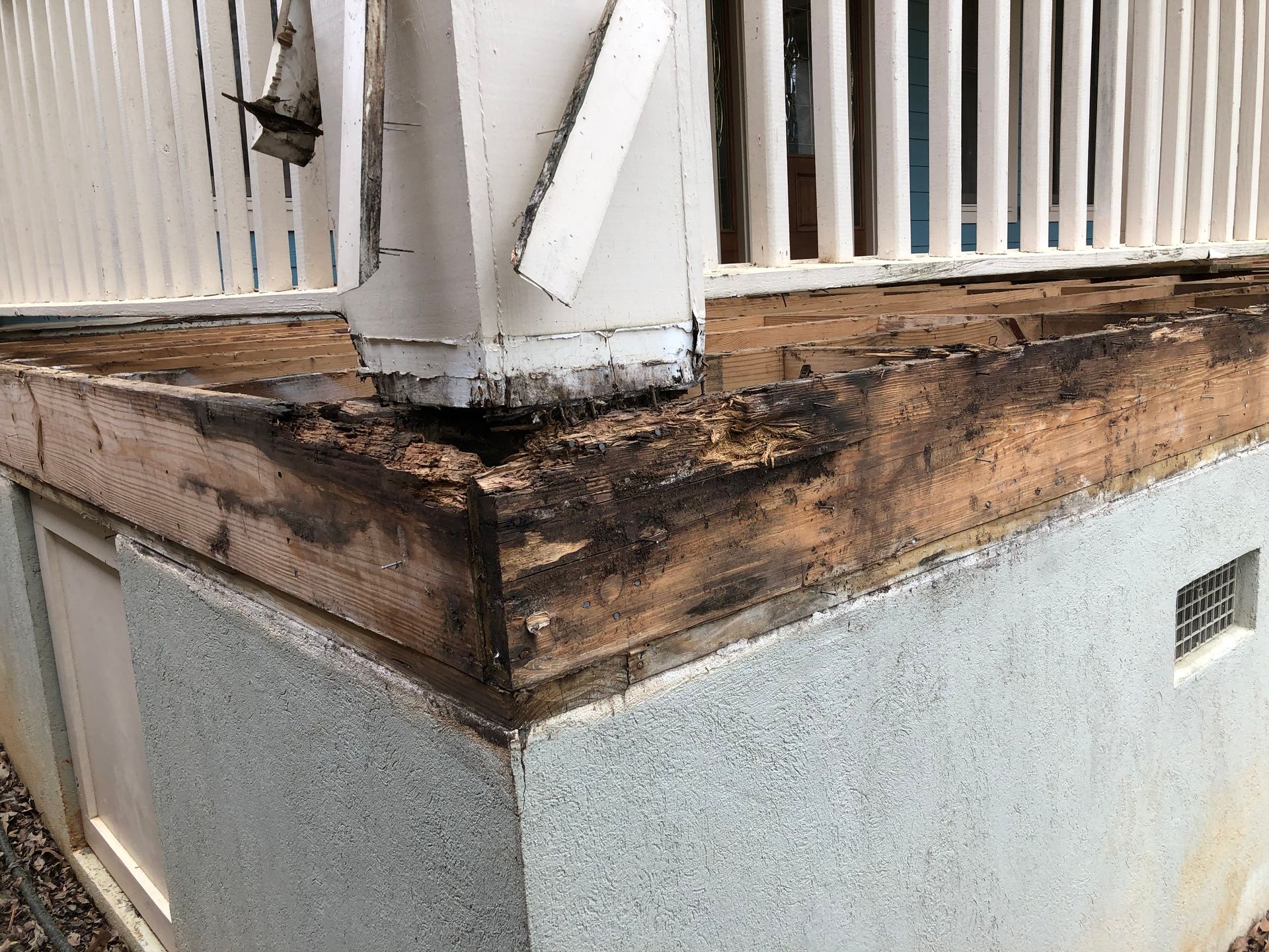 Weathered building corner with peeling brown trim and white siding, showing water damage and decay