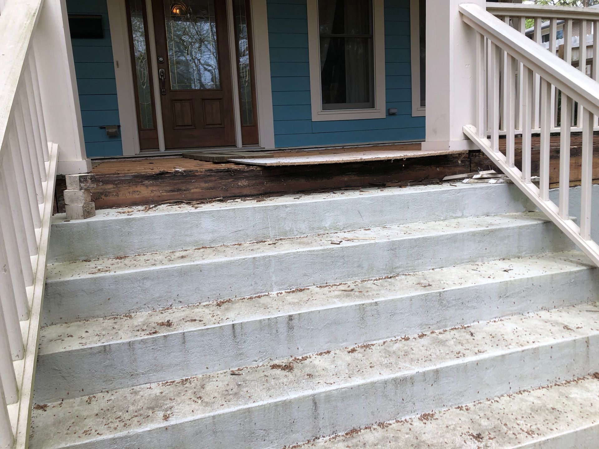 White concrete front steps with white railings leading to a blue house porch.