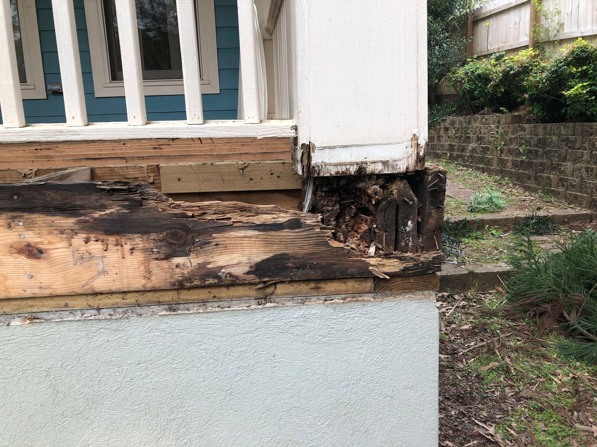 Damaged wooden house corner with rotting boards and exposed foundation by a grassy yard