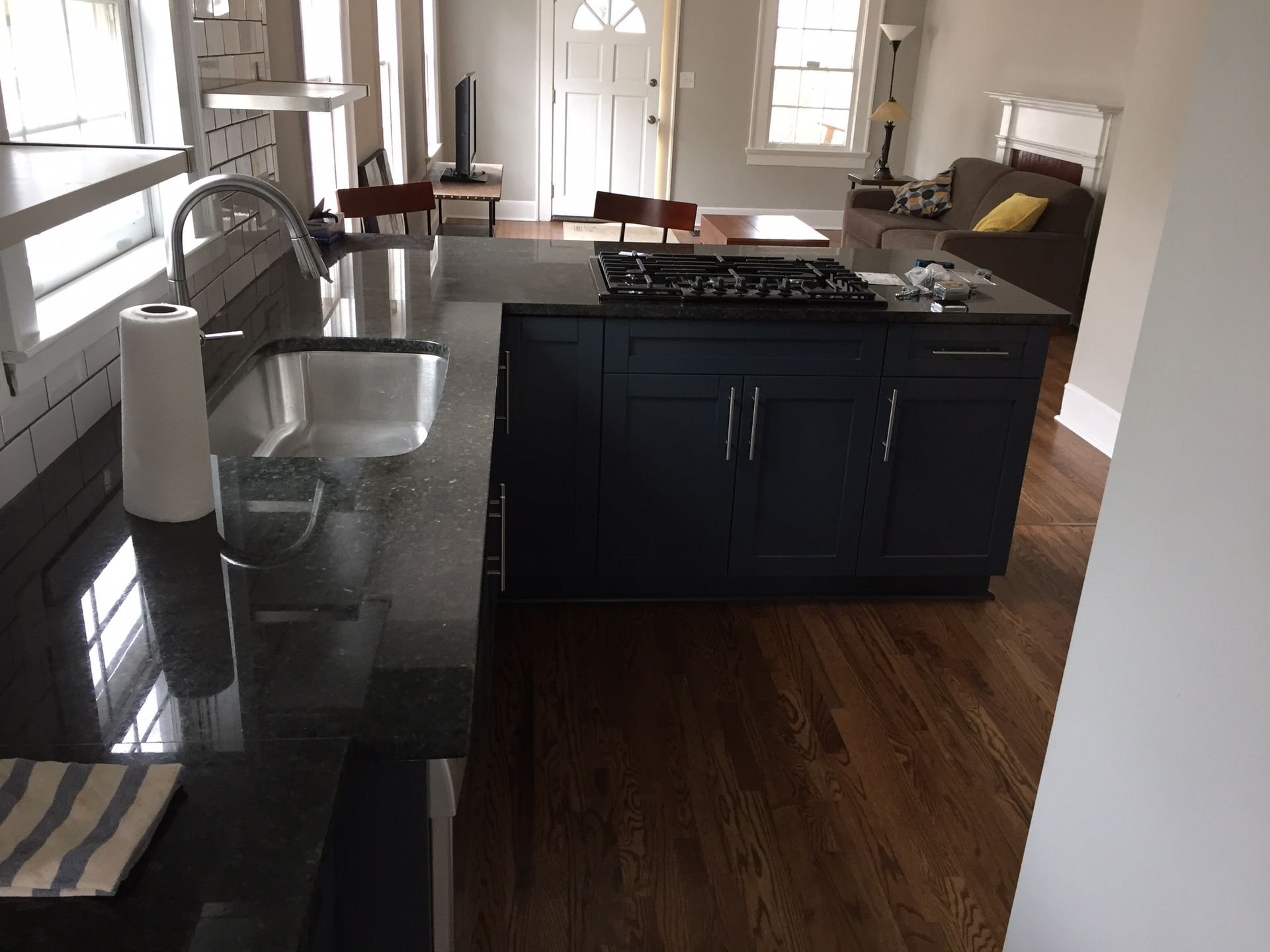 Modern kitchen with black island, granite countertop, sink, and bright windows overlooking a living area