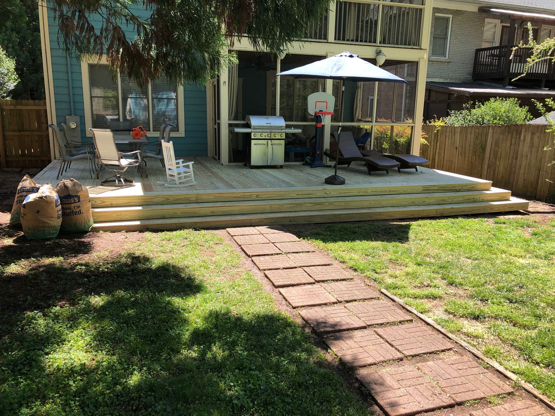 Backyard patio with deck chairs, umbrella, grill, and brick path leading across the lawn