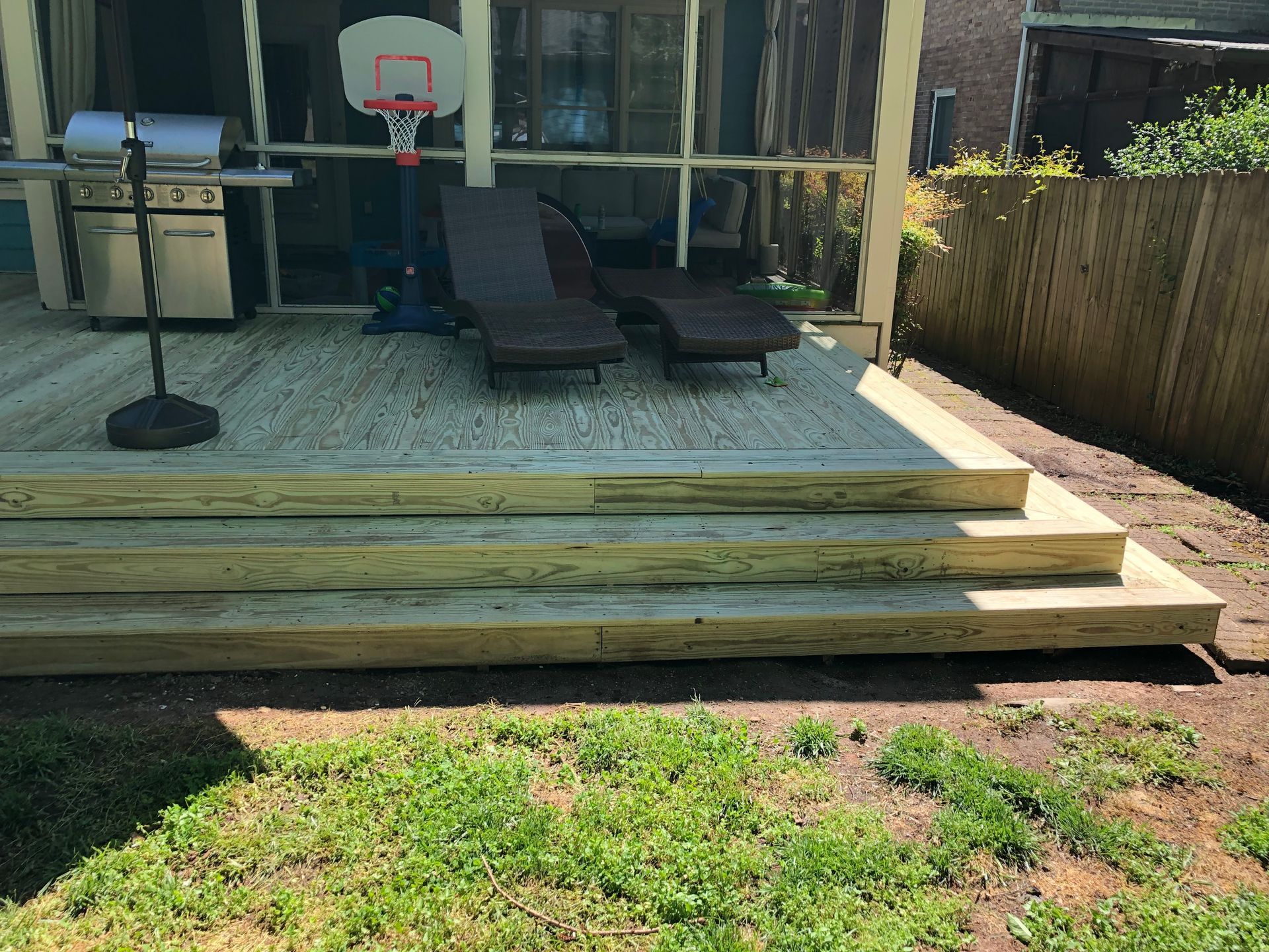 Backyard deck with steps, lounge chair, basketball hoop, and small table by a glass-walled house