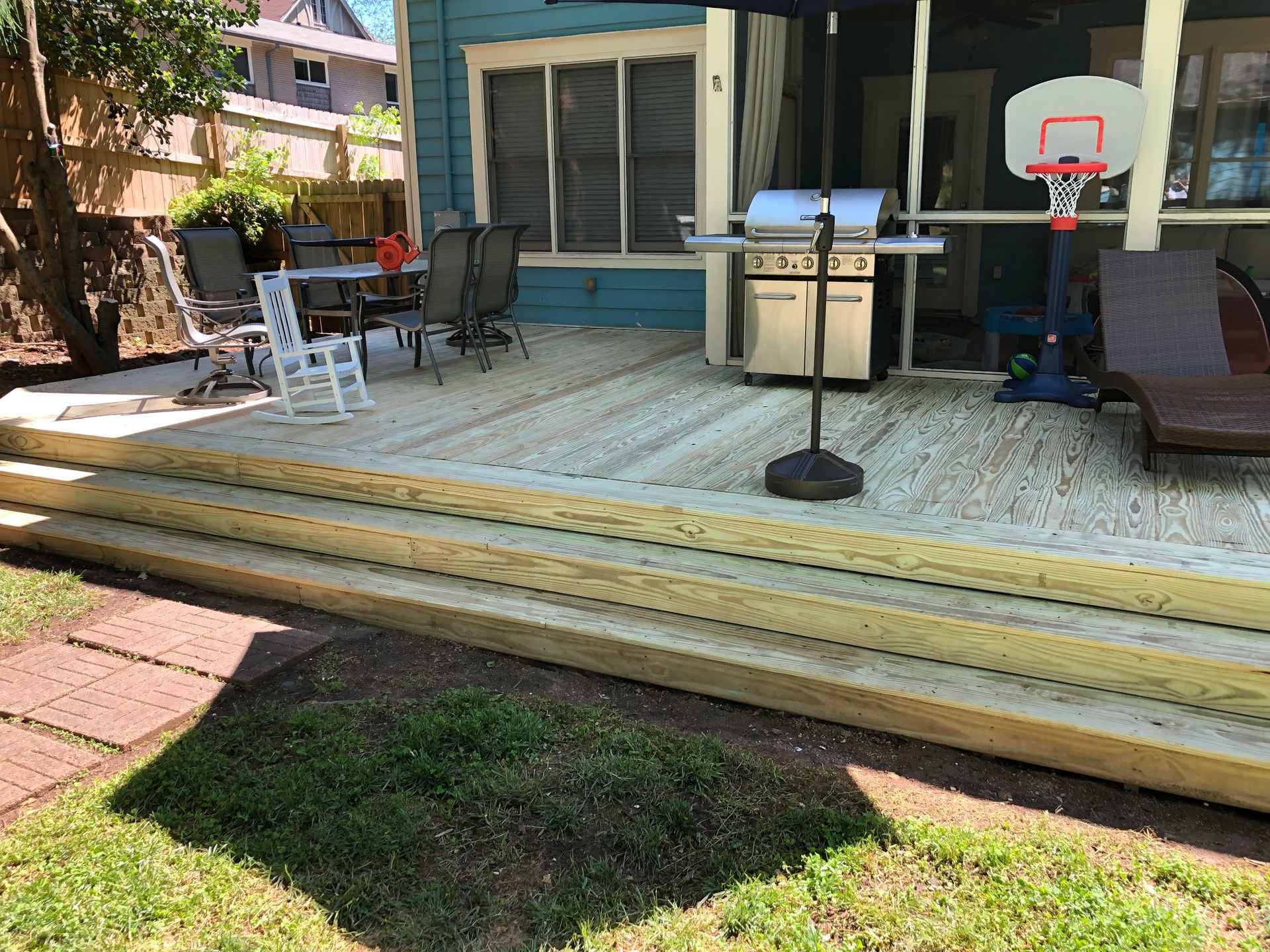 Backyard deck with grill, patio chairs, and a small basketball hoop beside a lawn