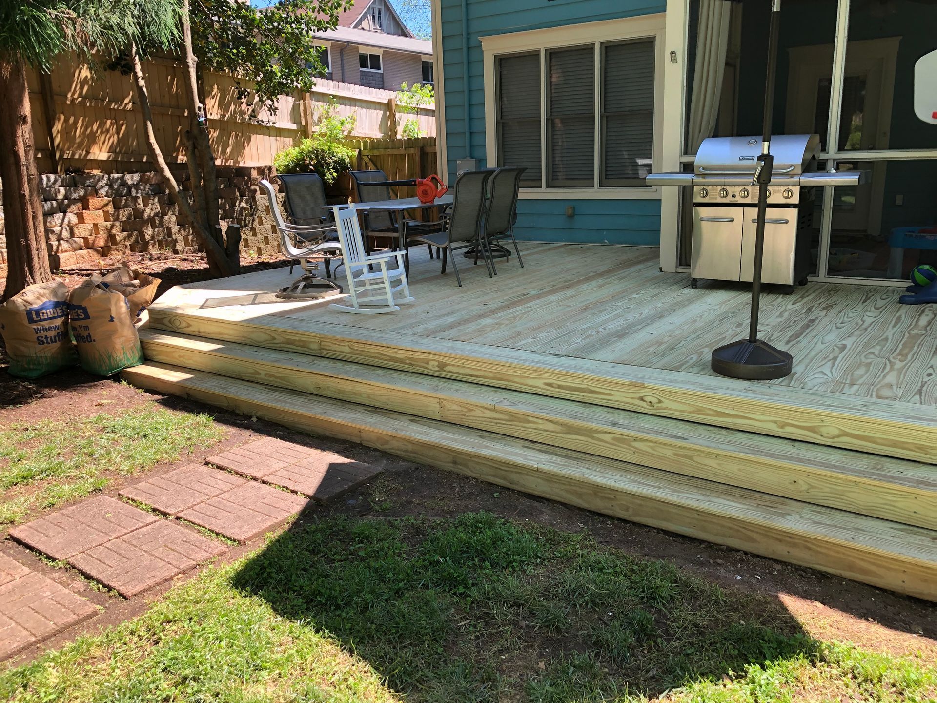 Back patio with beige steps, teal siding, grill, and patio chairs in a sunny yard