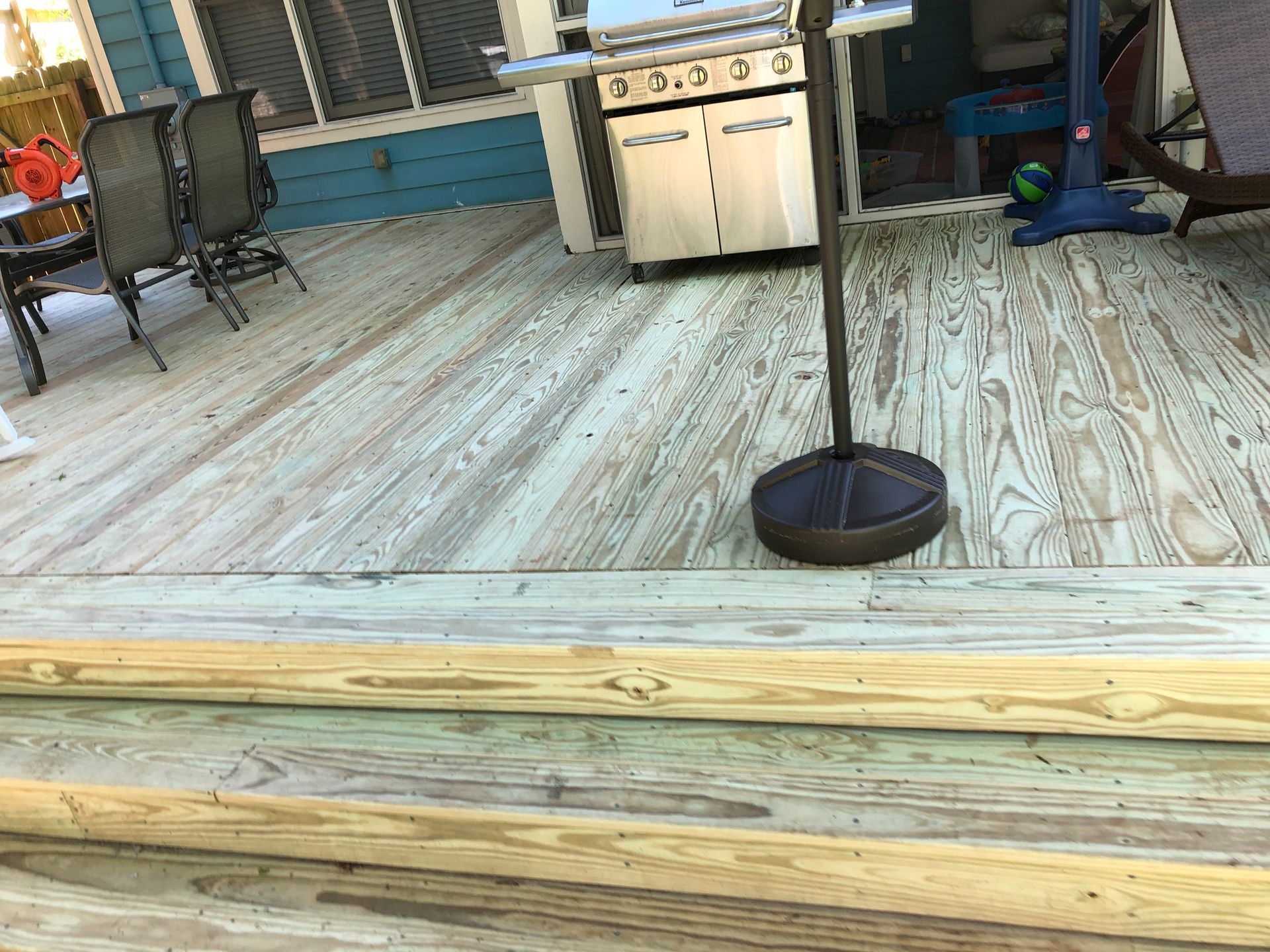 Patio deck with a black umbrella stand, grill, and chairs in front of a house