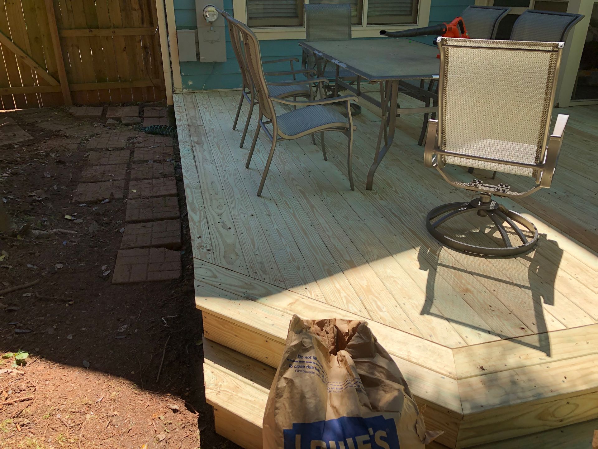Backyard deck with patio table and chairs, a wooden chair, and a shopping bag on the steps