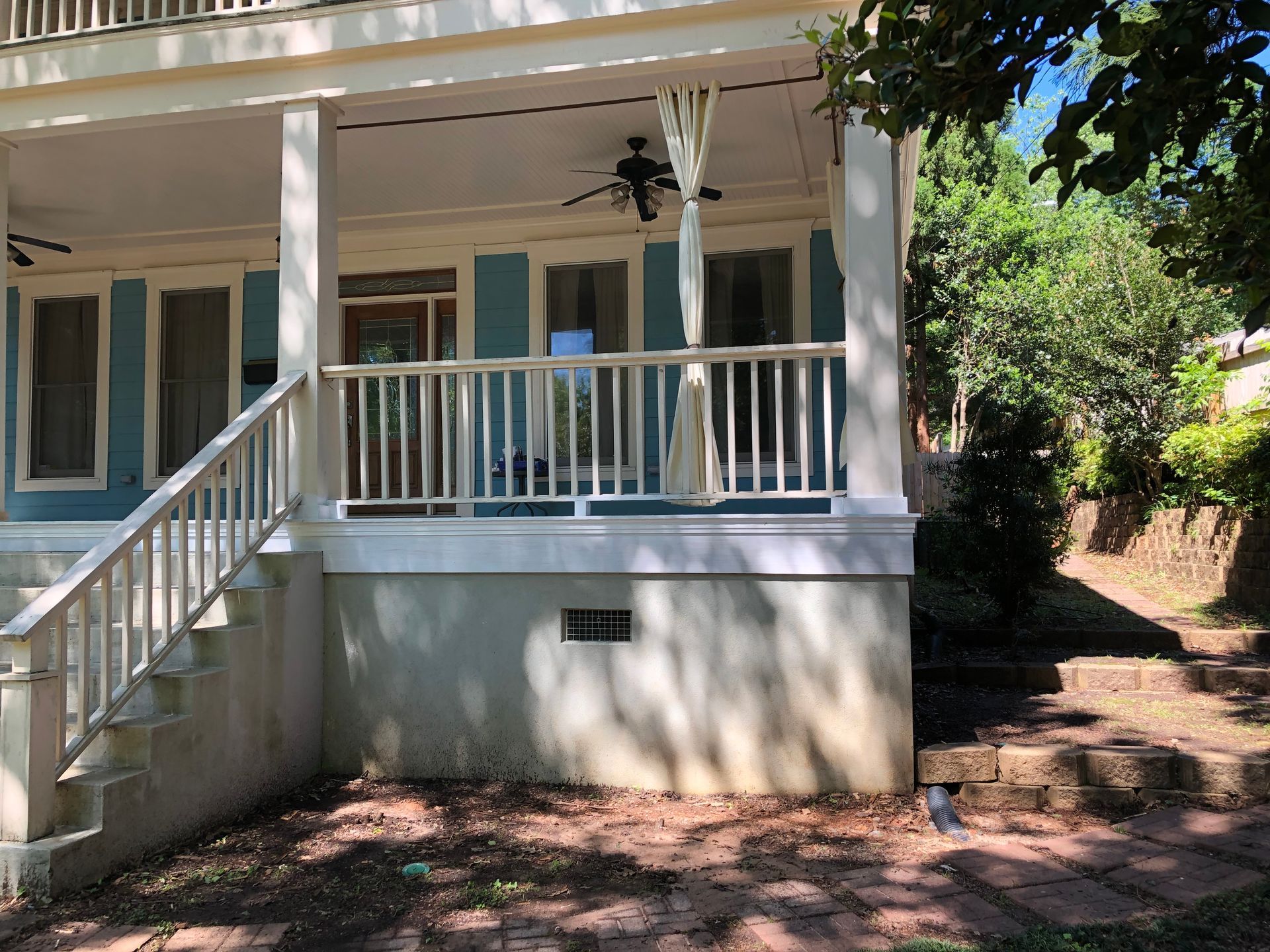Front porch of a white house with columns, steps, and shaded trees beside it