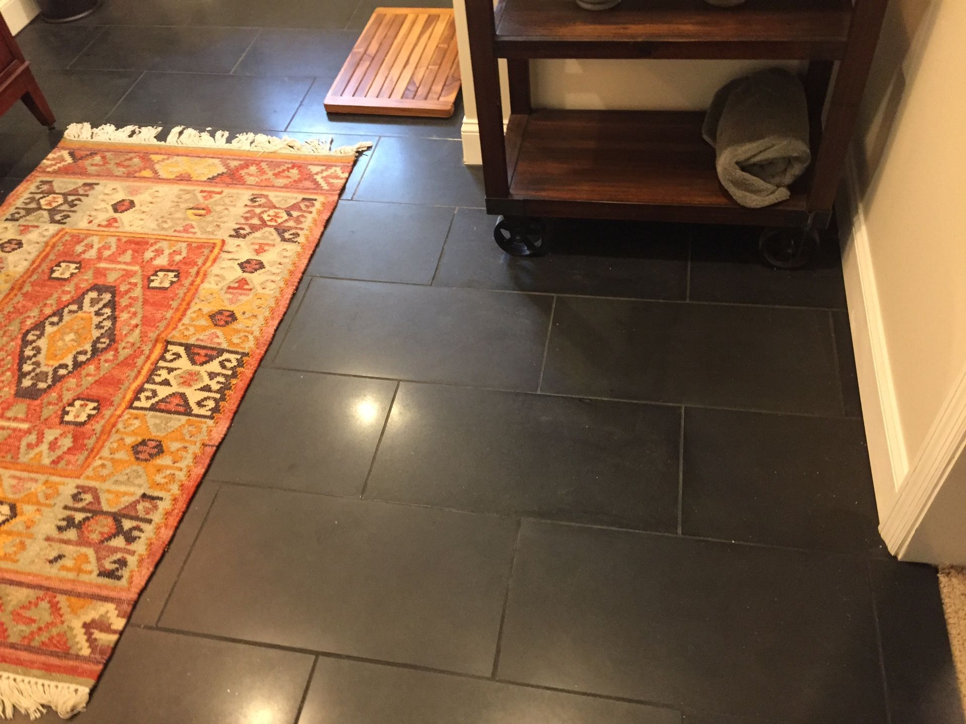 Dark tiled floor beside a red patterned rug and a small wooden shelf in a hallway