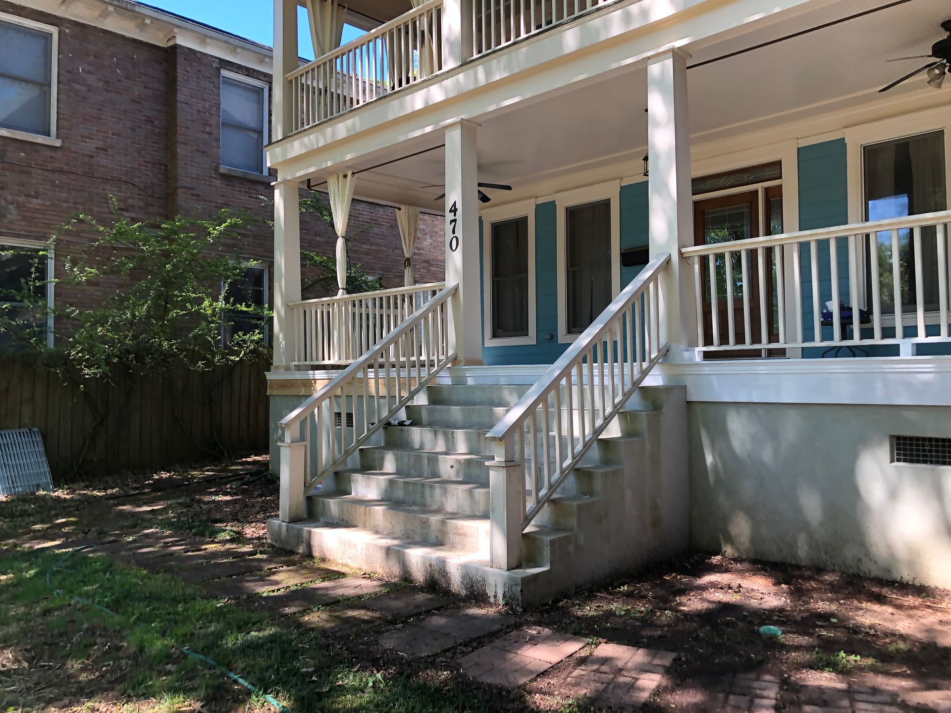 Back porch with white railings, steps, and covered patio beside a brick house