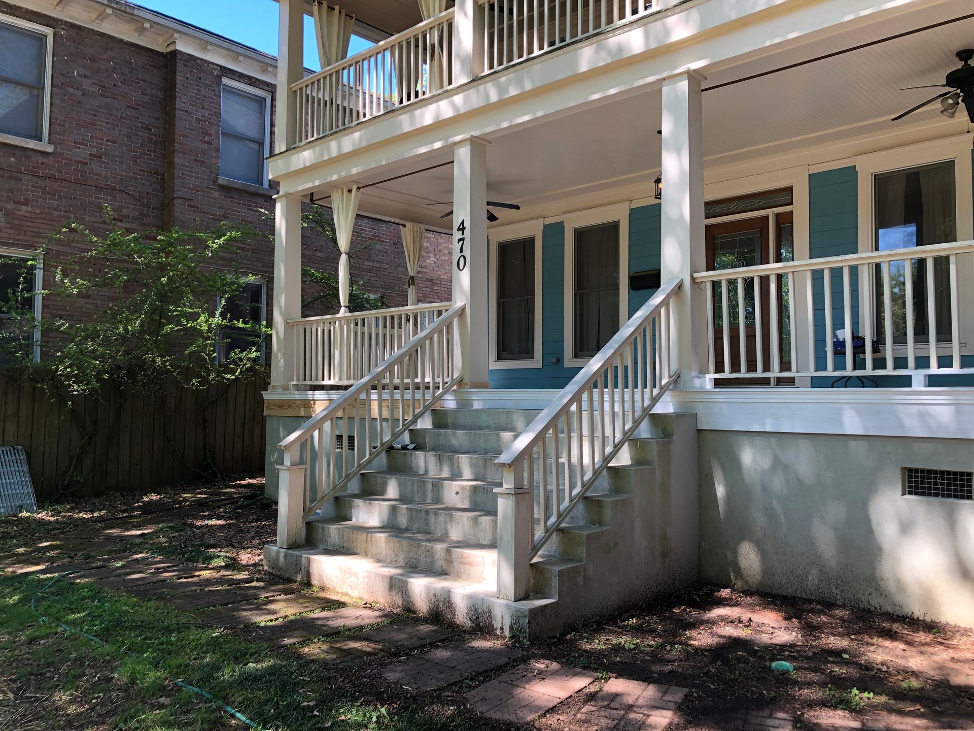 Front porch of a white house with teal doors, stairs, and railings in a shaded yard