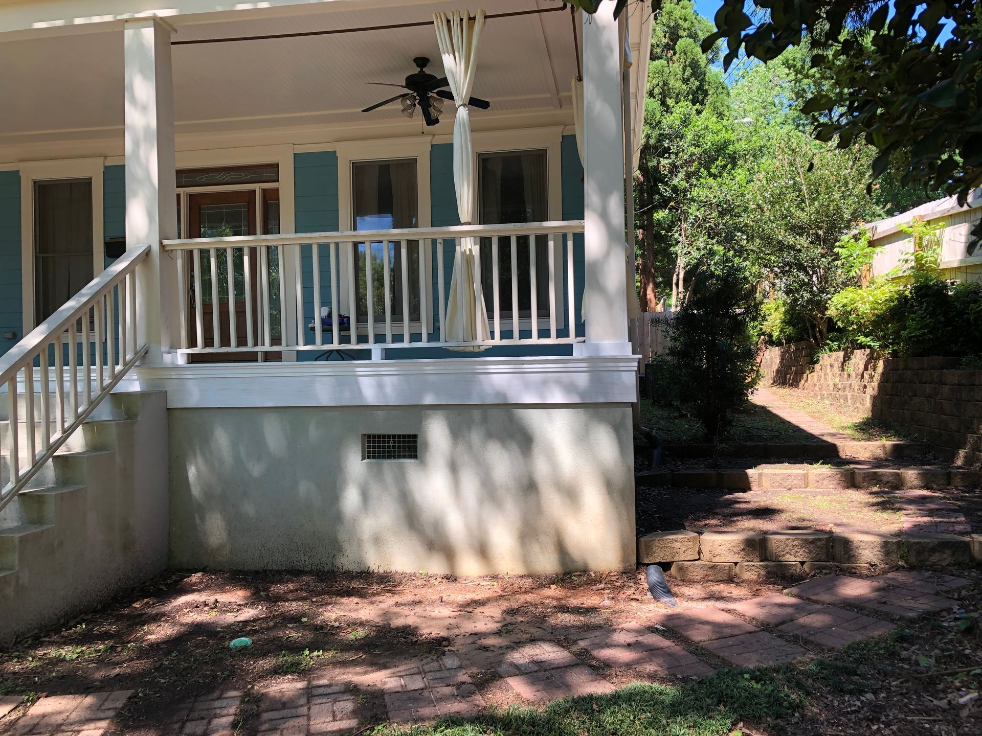 Front porch of a house with white railings, stairs, and shaded yard with trees and brick path