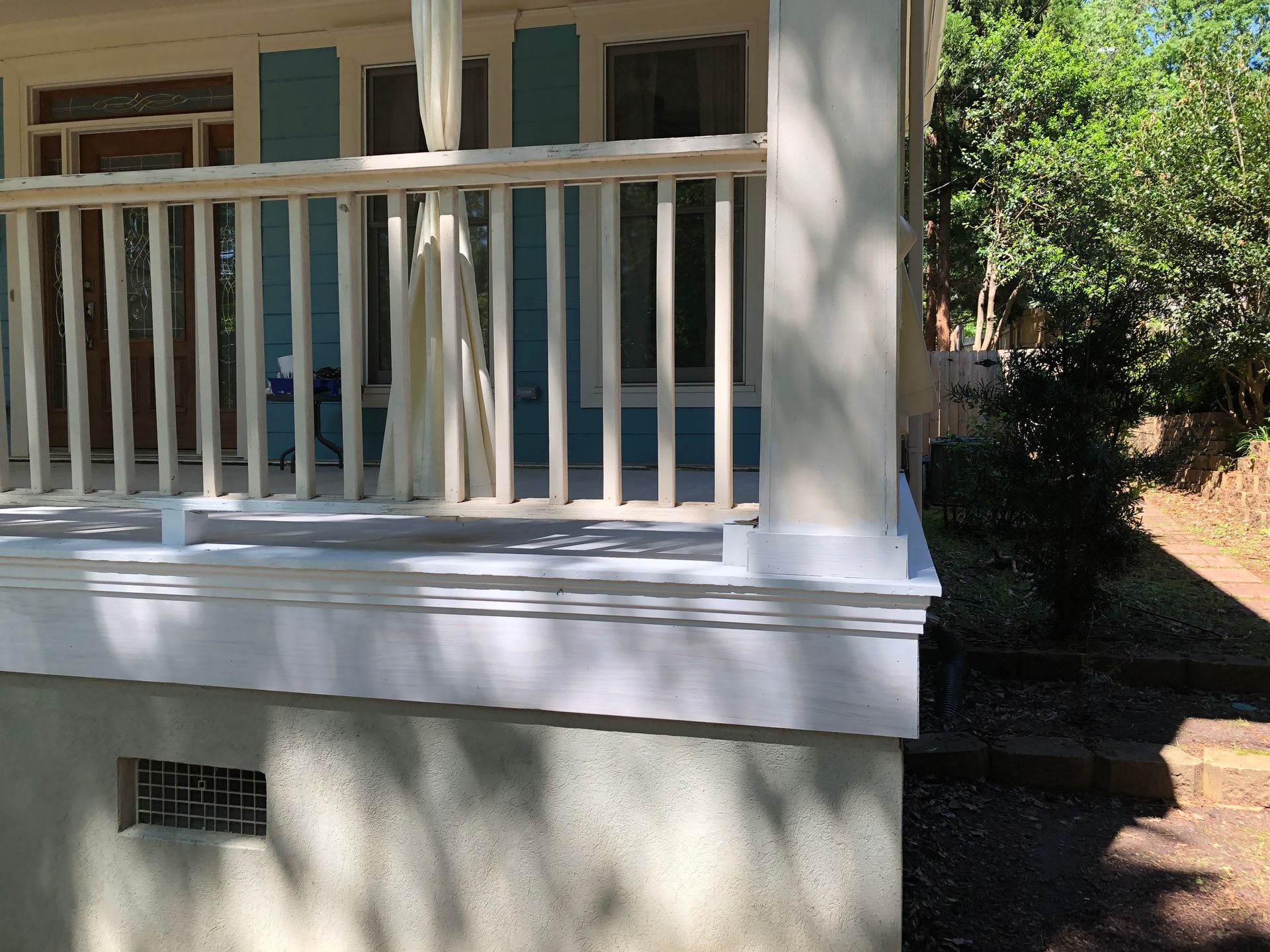 White porch railing and columns on a house with blue doors and a shaded walkway beside it