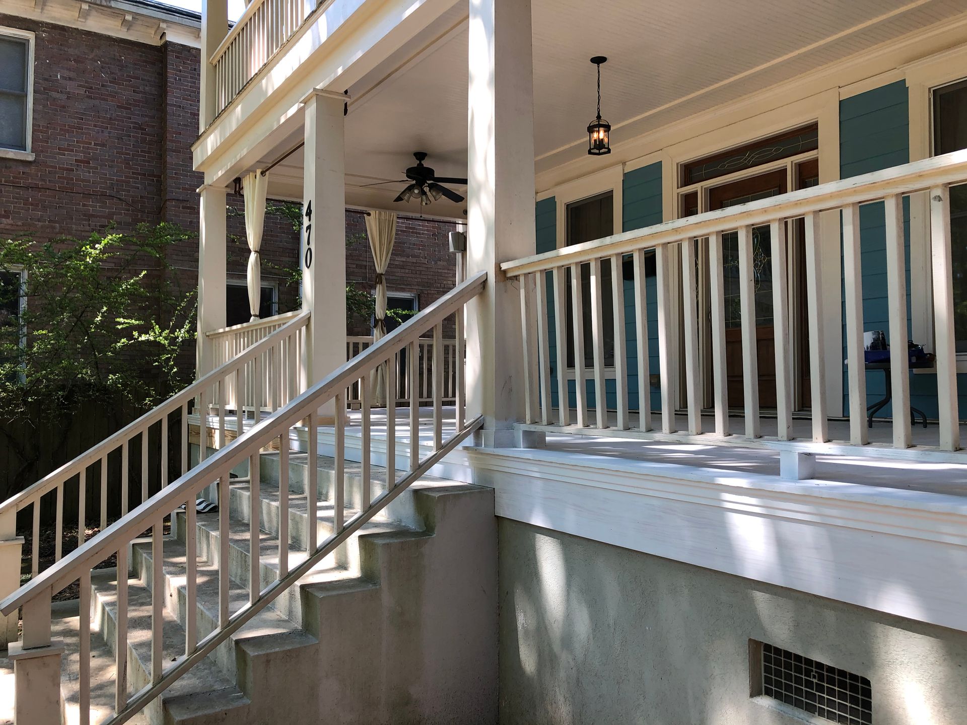 Porch stairs and white railing leading to a shaded front porch of a house